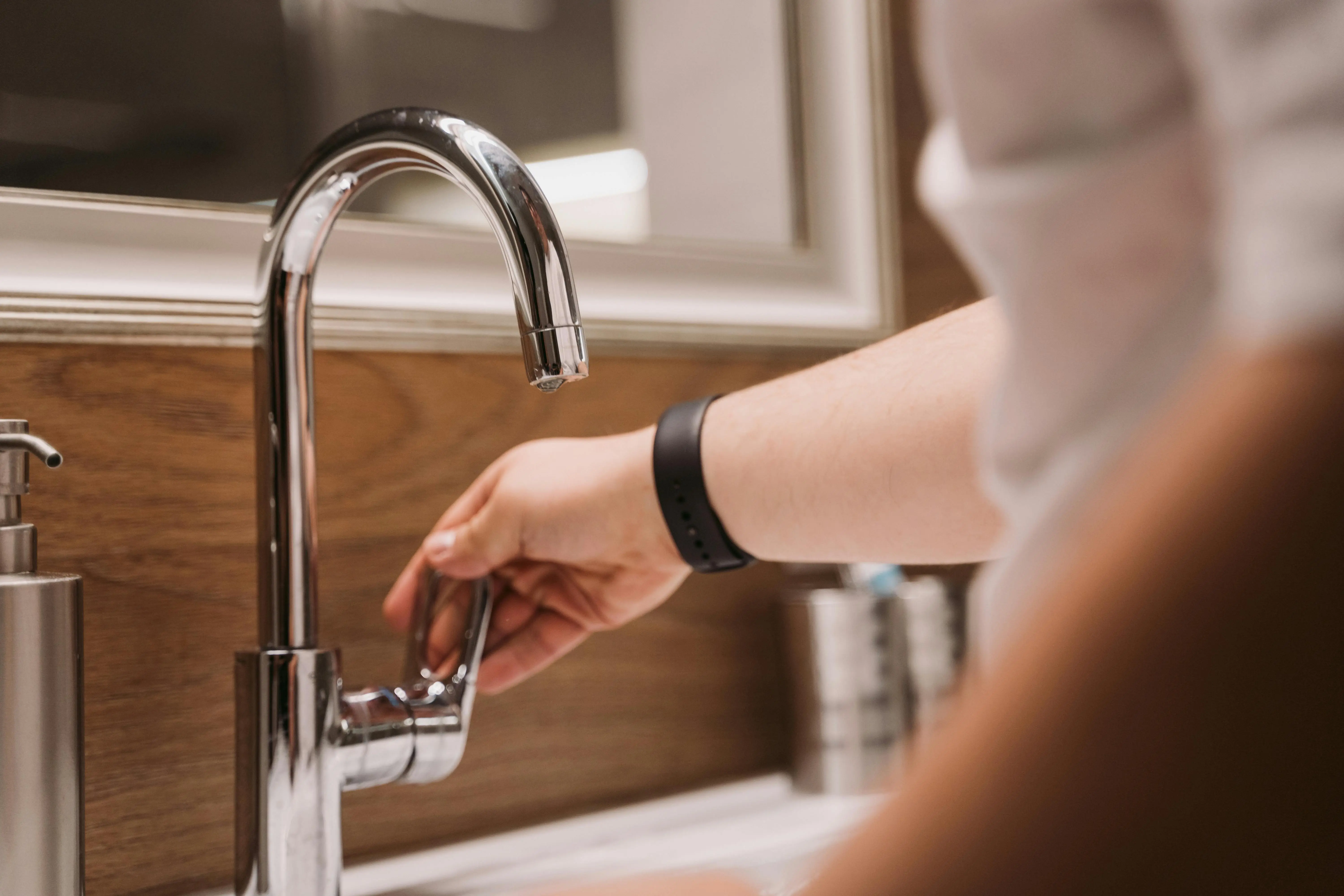 sink parts Close-up of a person's hand turning a chrome faucet handle in a modern bathroom setting.