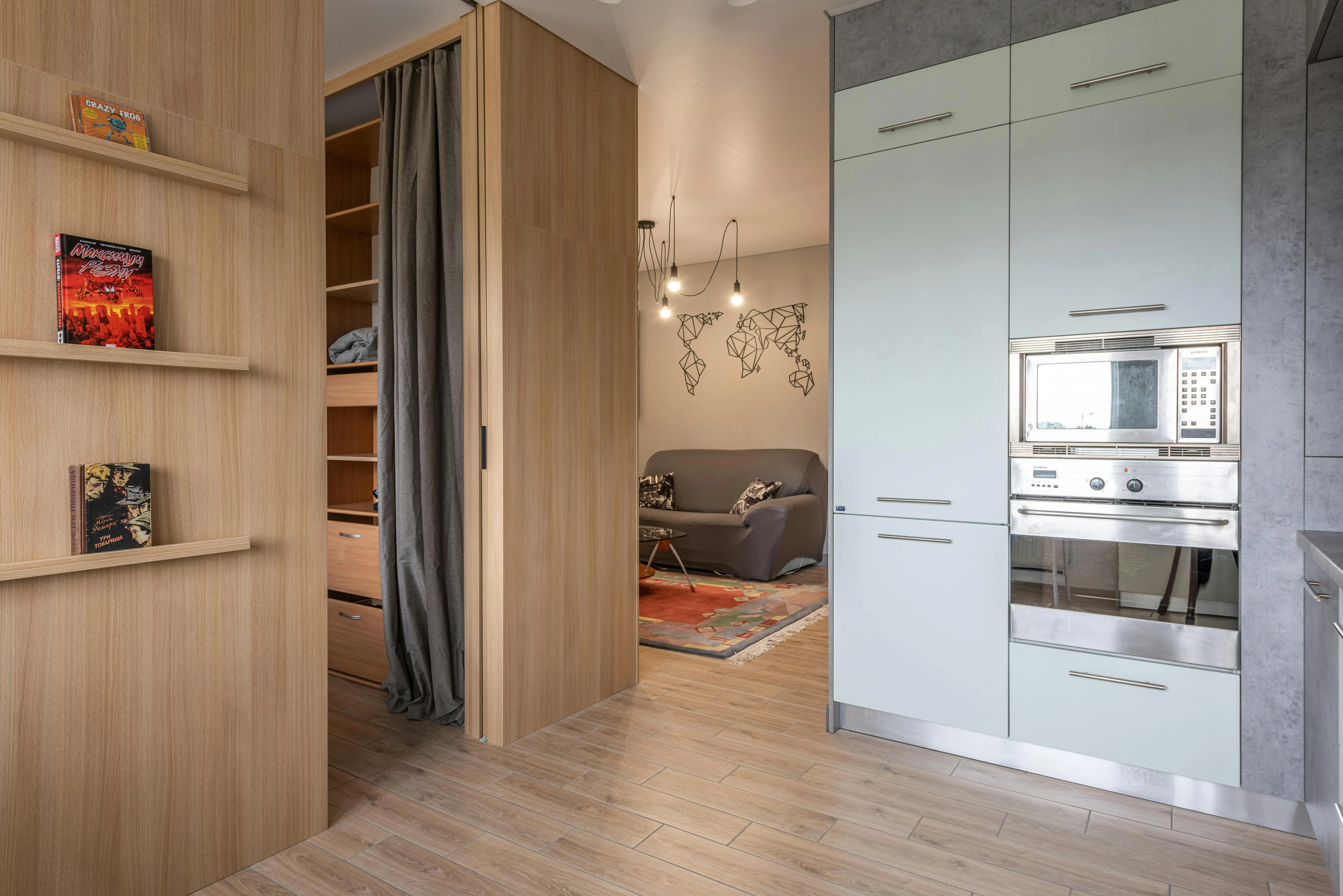 small sofa bed with storage Modern apartment with cabinets with oven and microwave in kitchen near wooden shelves with books near entrance in room with wardrobe with curtains near living room with couch and carpet
