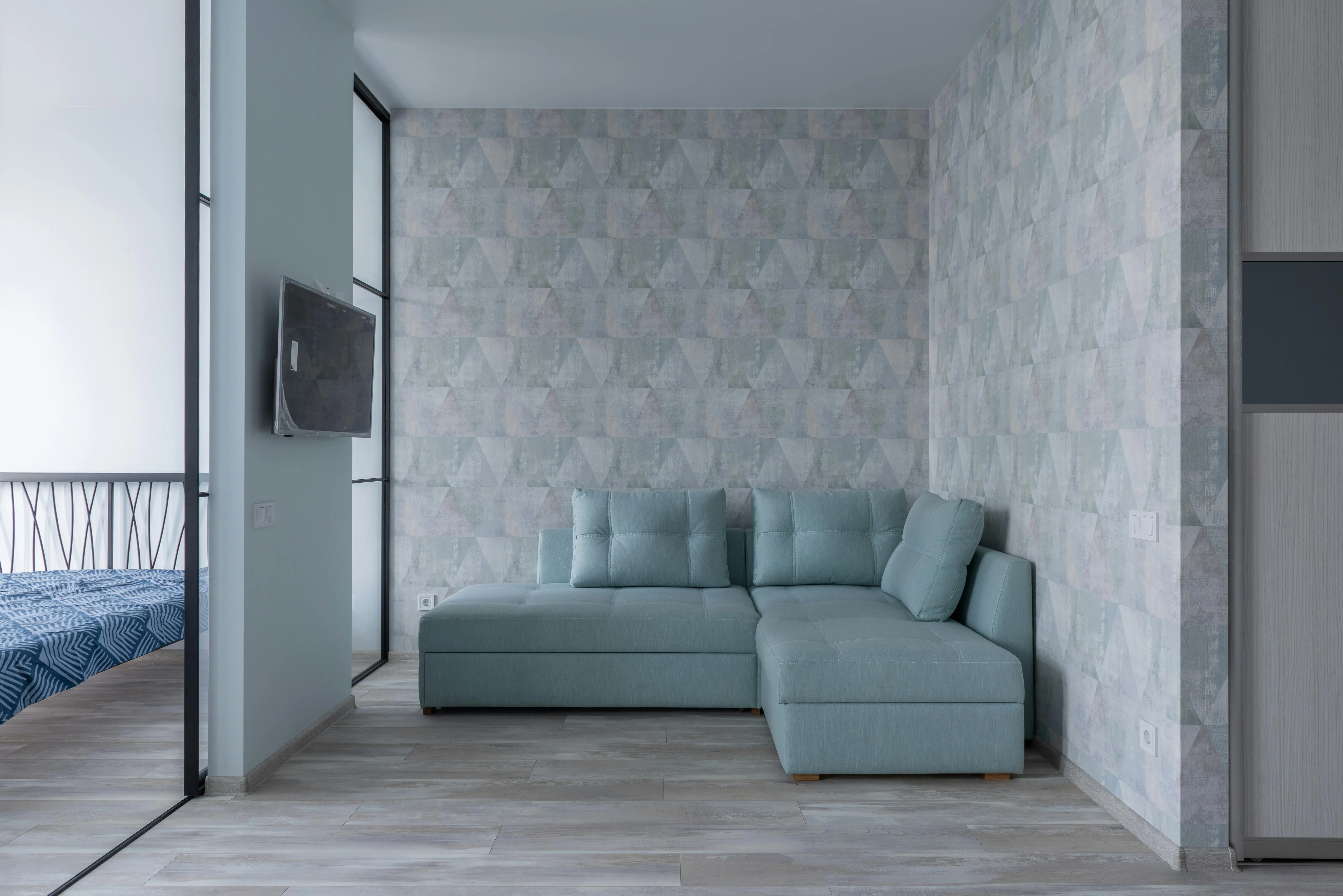 small sofa bed with storage Comfortable sofa with cushions placed near wall with wallpaper and bedroom with glass wall and bed in modern flat with TV