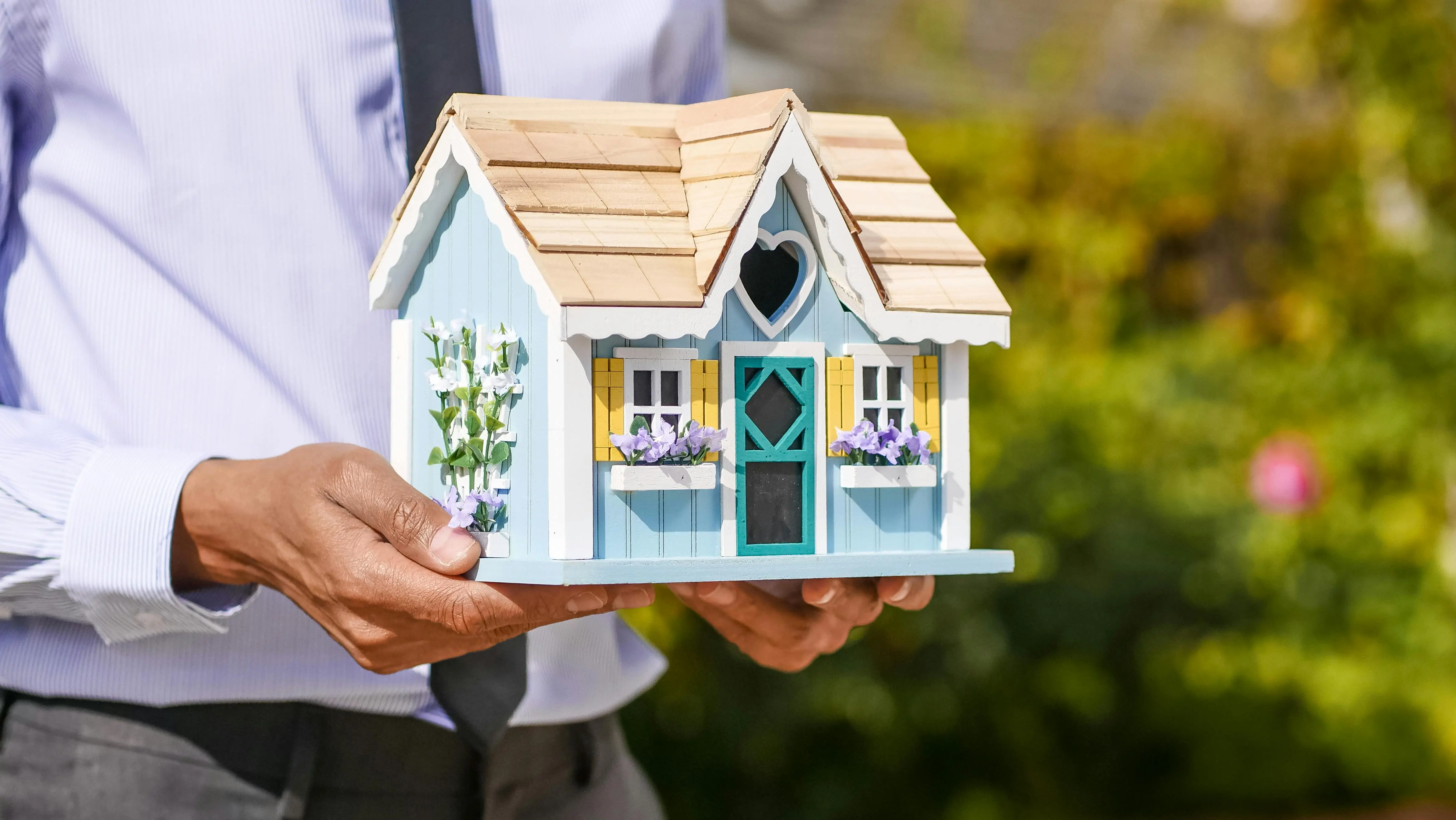 tiny home tips Close-up of a person holding a decorative miniature house outdoors.