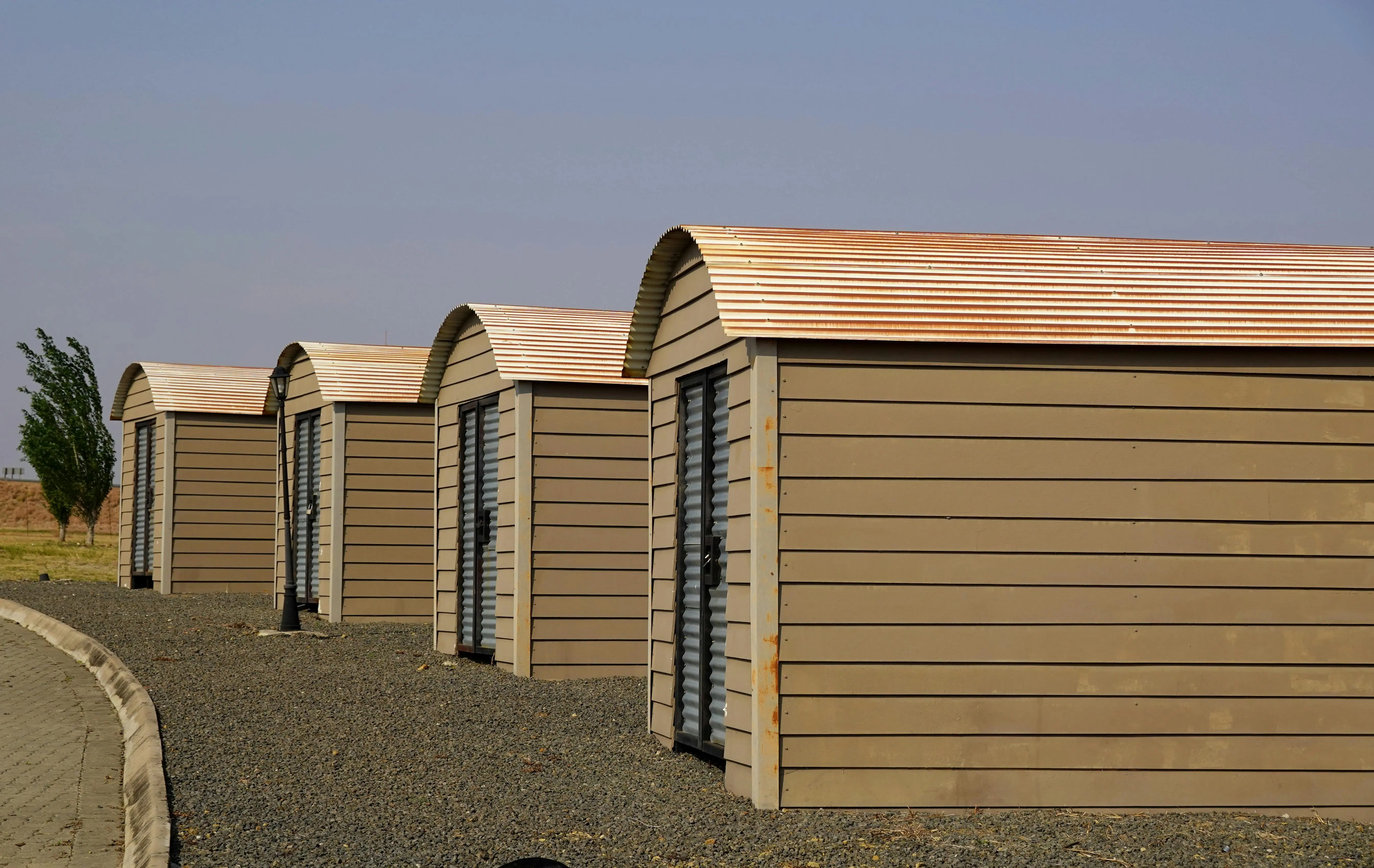 tiny home tips and tricks Four identical modern storage sheds aligned on a gravel surface with clear skies.