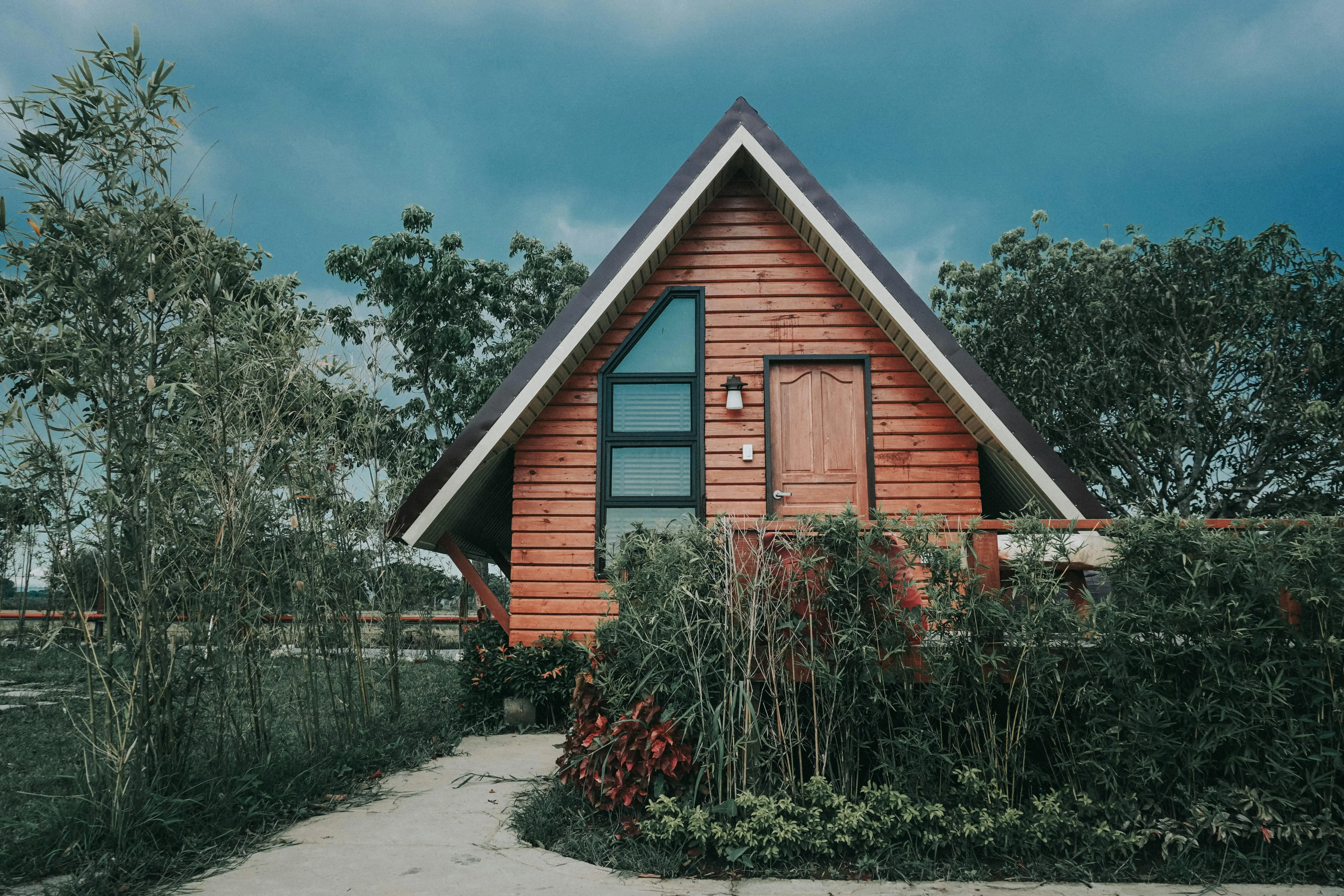living in a tiny home tips Cozy wooden A-frame tiny house surrounded by lush greenery and vibrant plants outdoors.