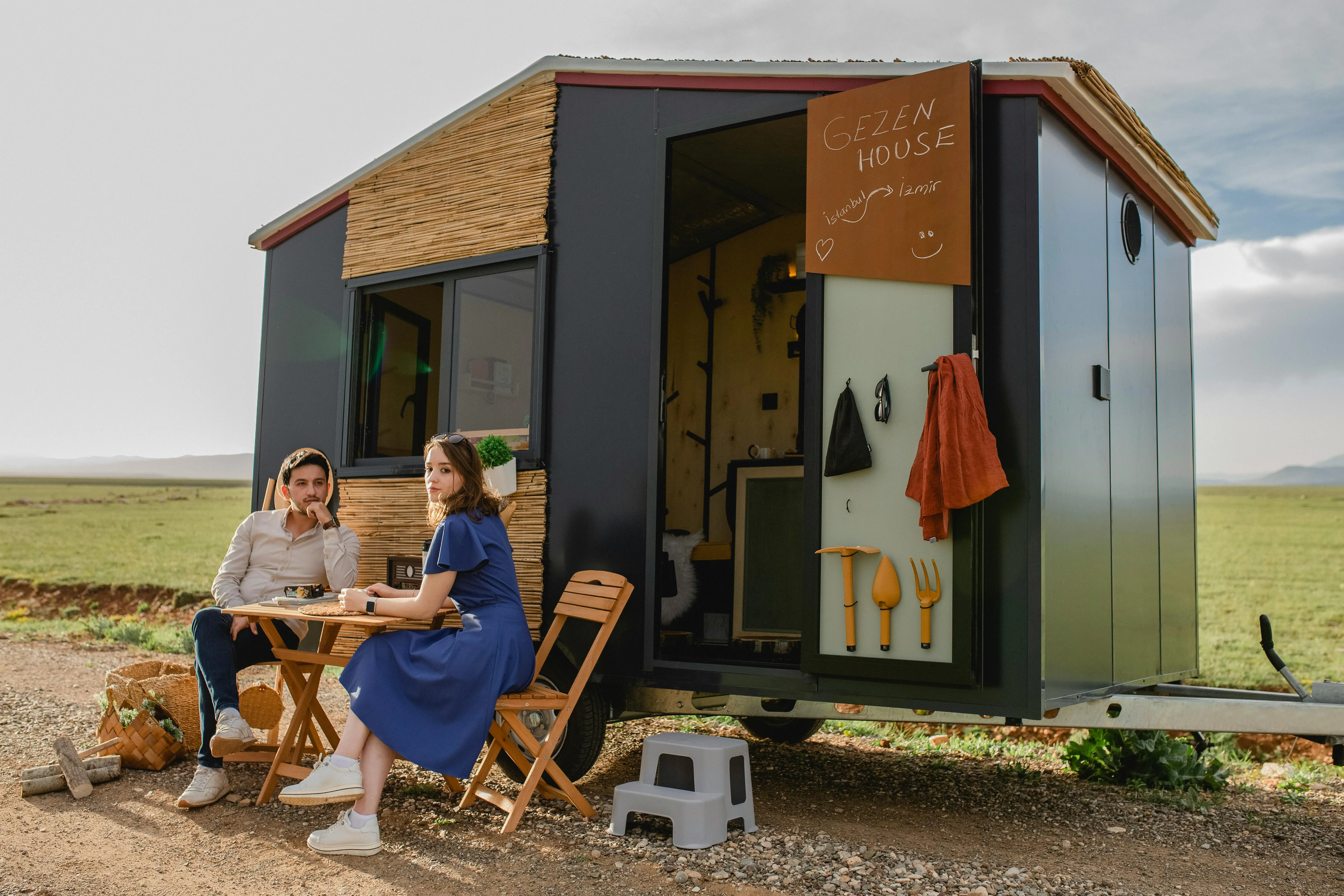 tiny house living tips A couple enjoys a relaxing day outdoors near a modern tiny house with chairs and a table.