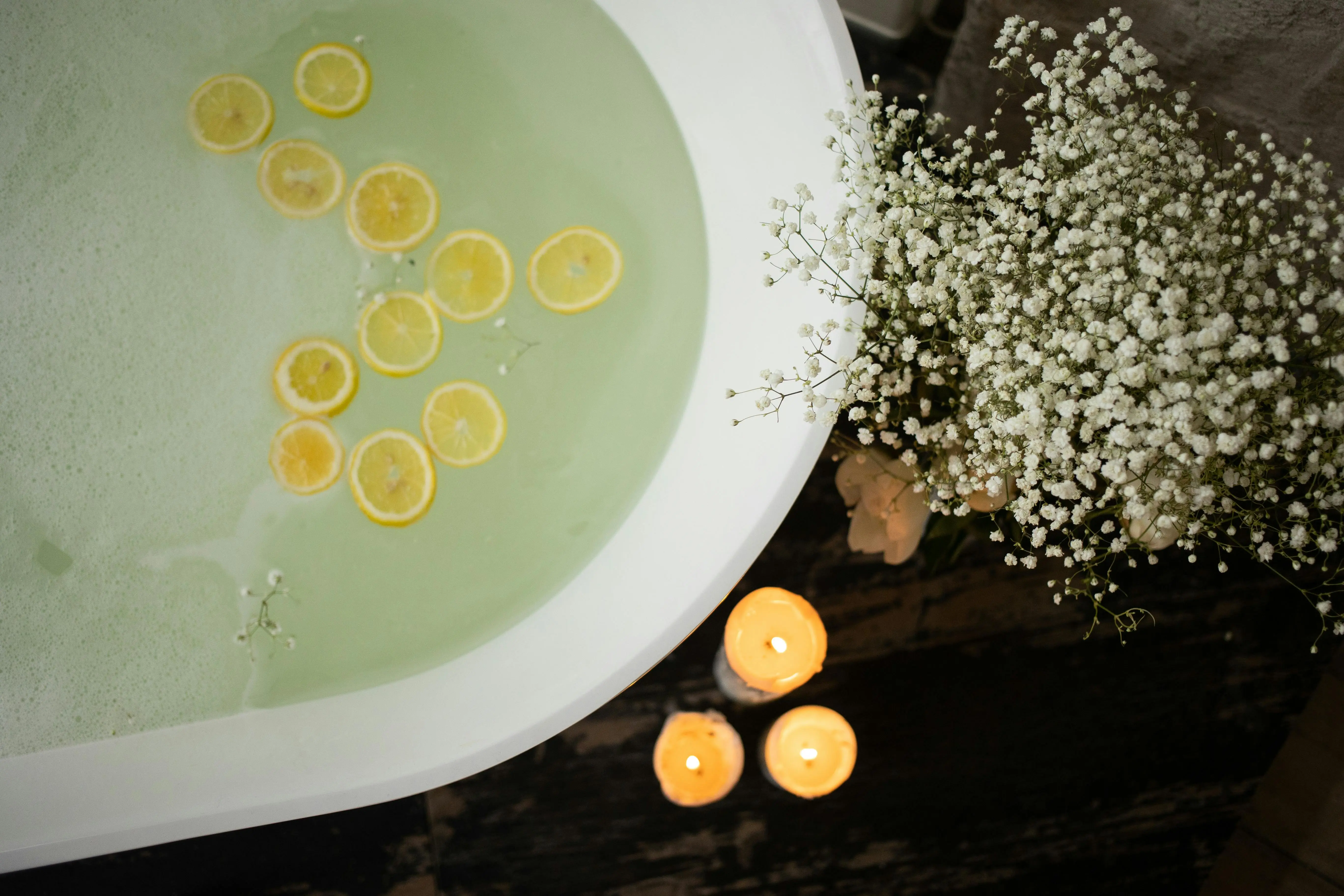 garden tubs Top view of white tub with lemon slices on water surface near burning candles and blooming flowers in modern bathroom