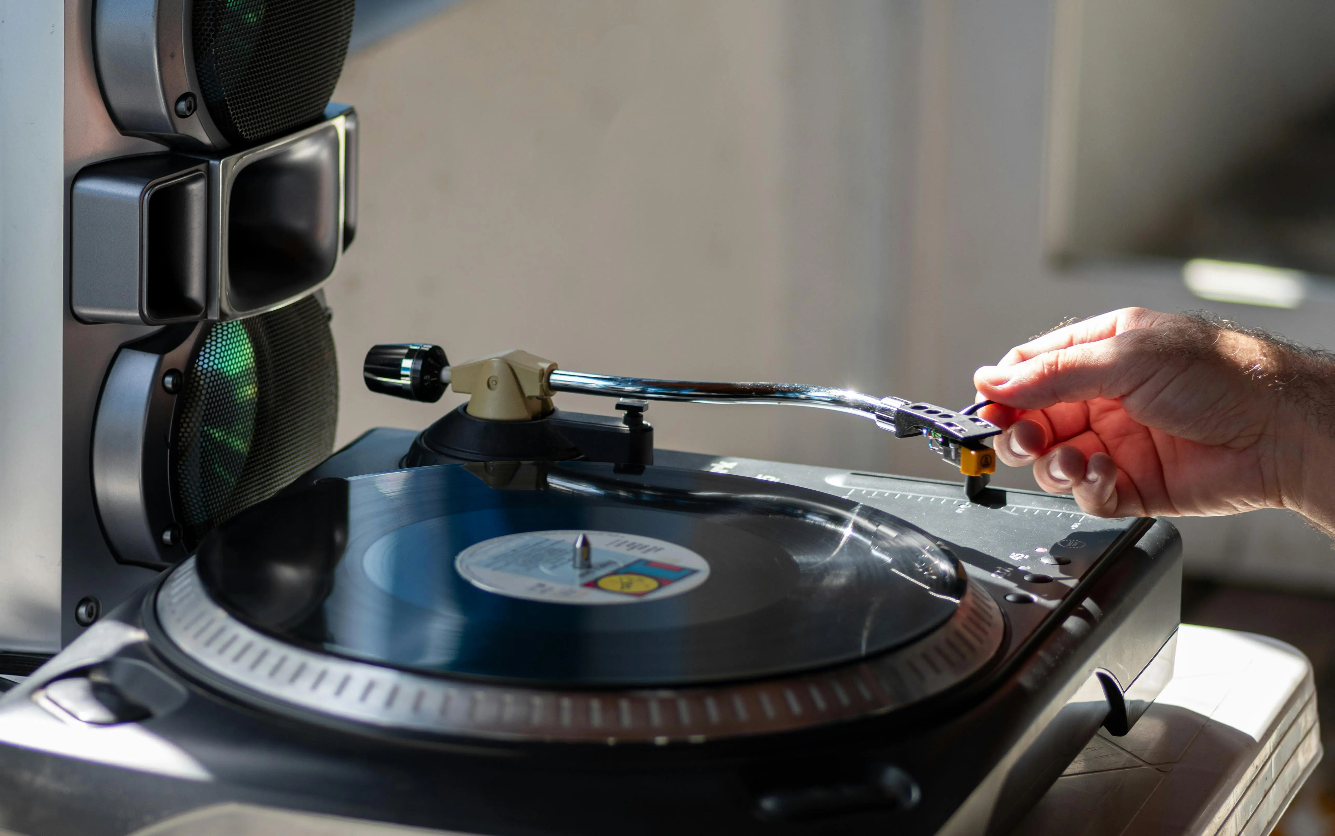 turntable and vinyl stand Close-up of a hand adjusting a needle on a vintage vinyl turntable next to speakers.
