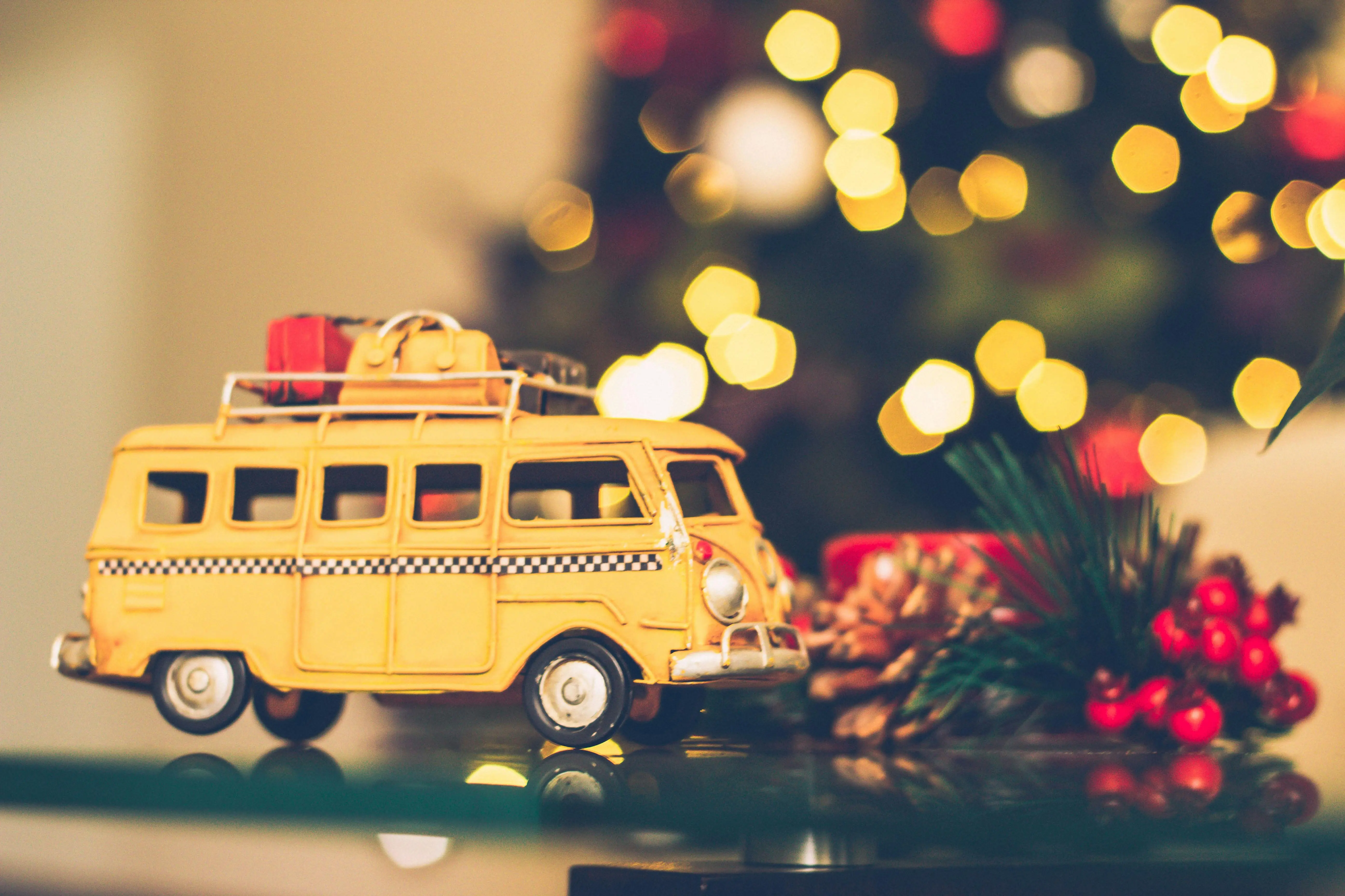 christmas holiday themes Festive yellow toy van with Christmas tree decor and bokeh lights, evoking travel and holiday spirit.