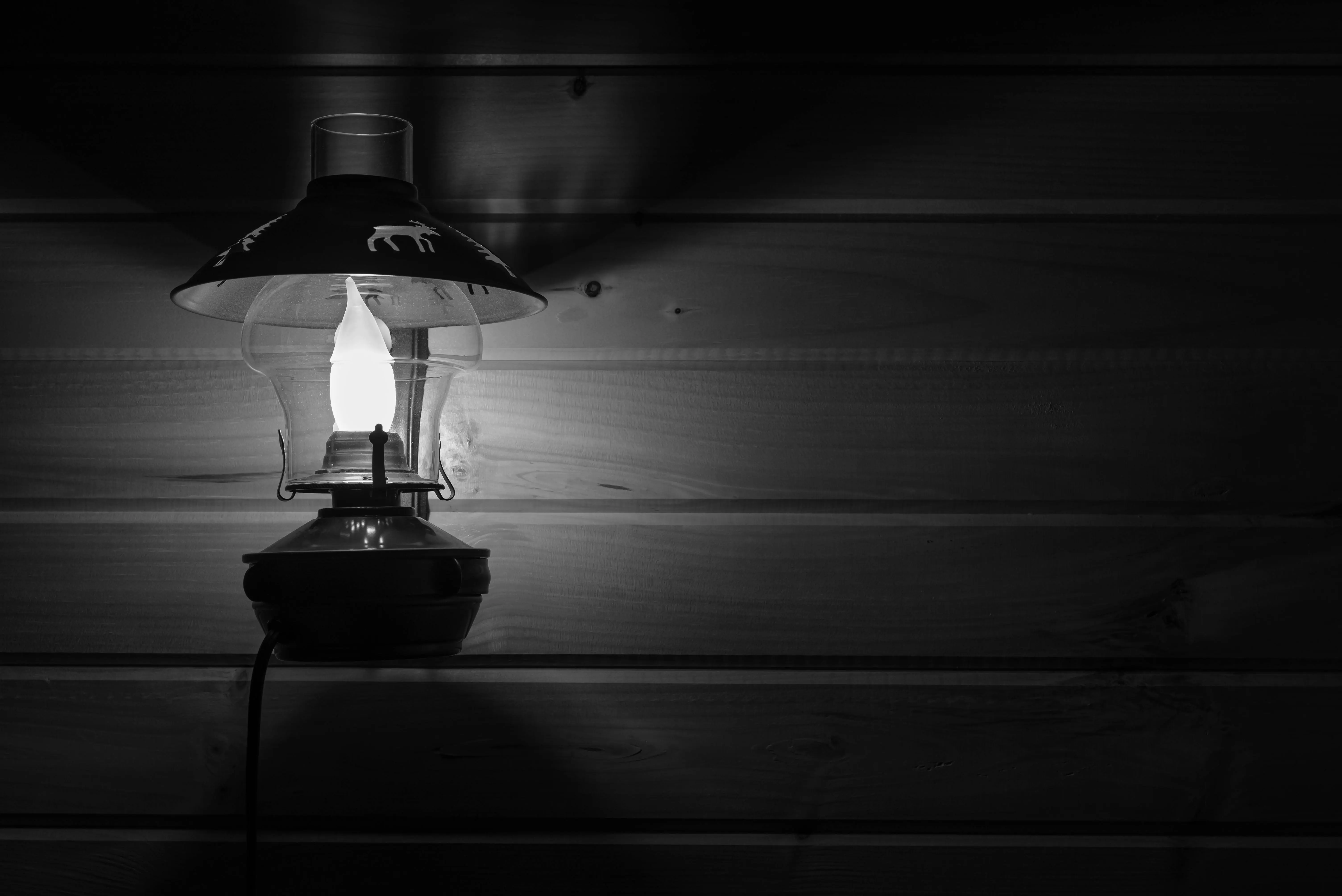 white lamp Black and white photo of a vintage lamp illuminated against a wooden wall interior setting.