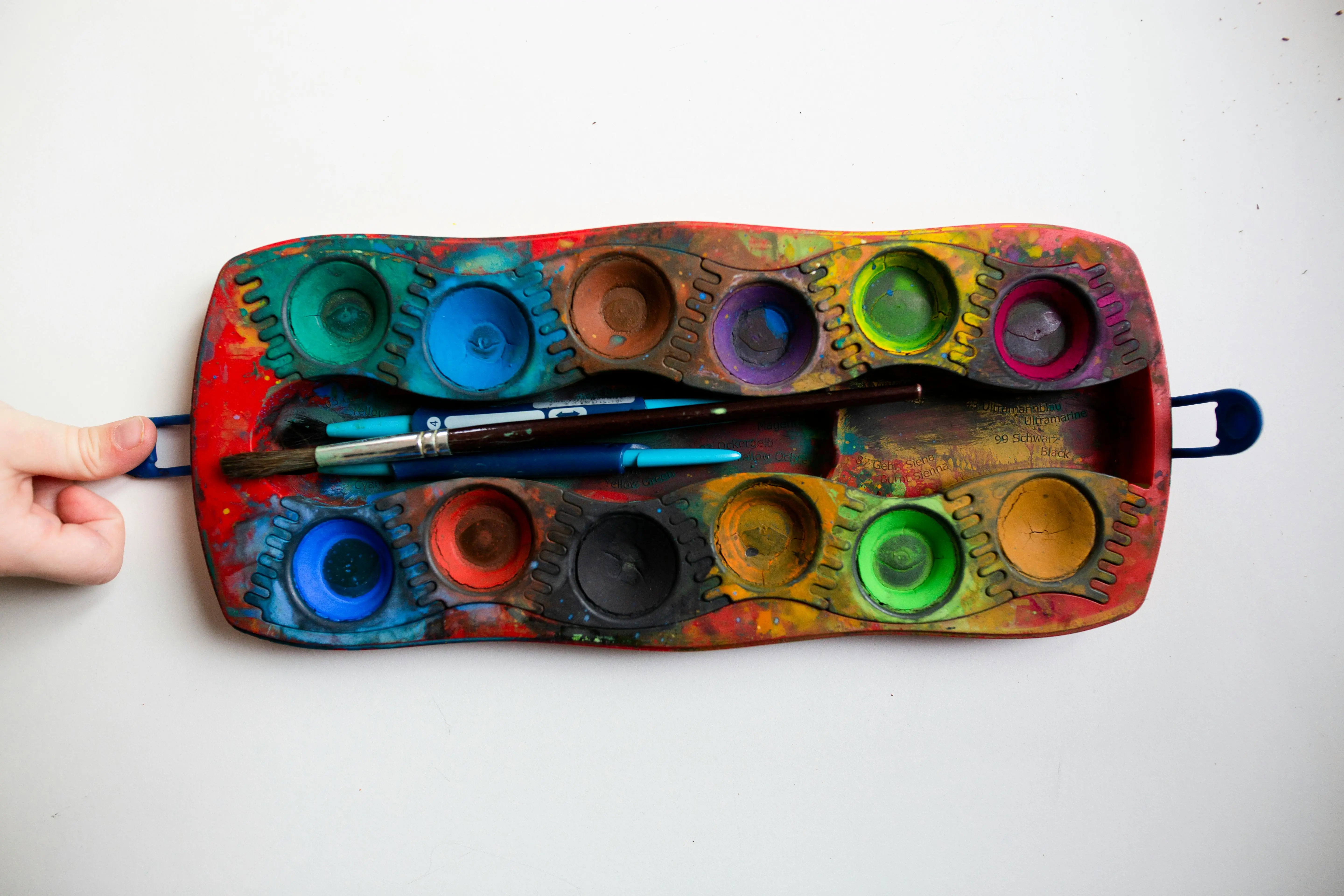 watercolor paint set A colorful watercolor palette with various paint wells and brushes on a white surface.