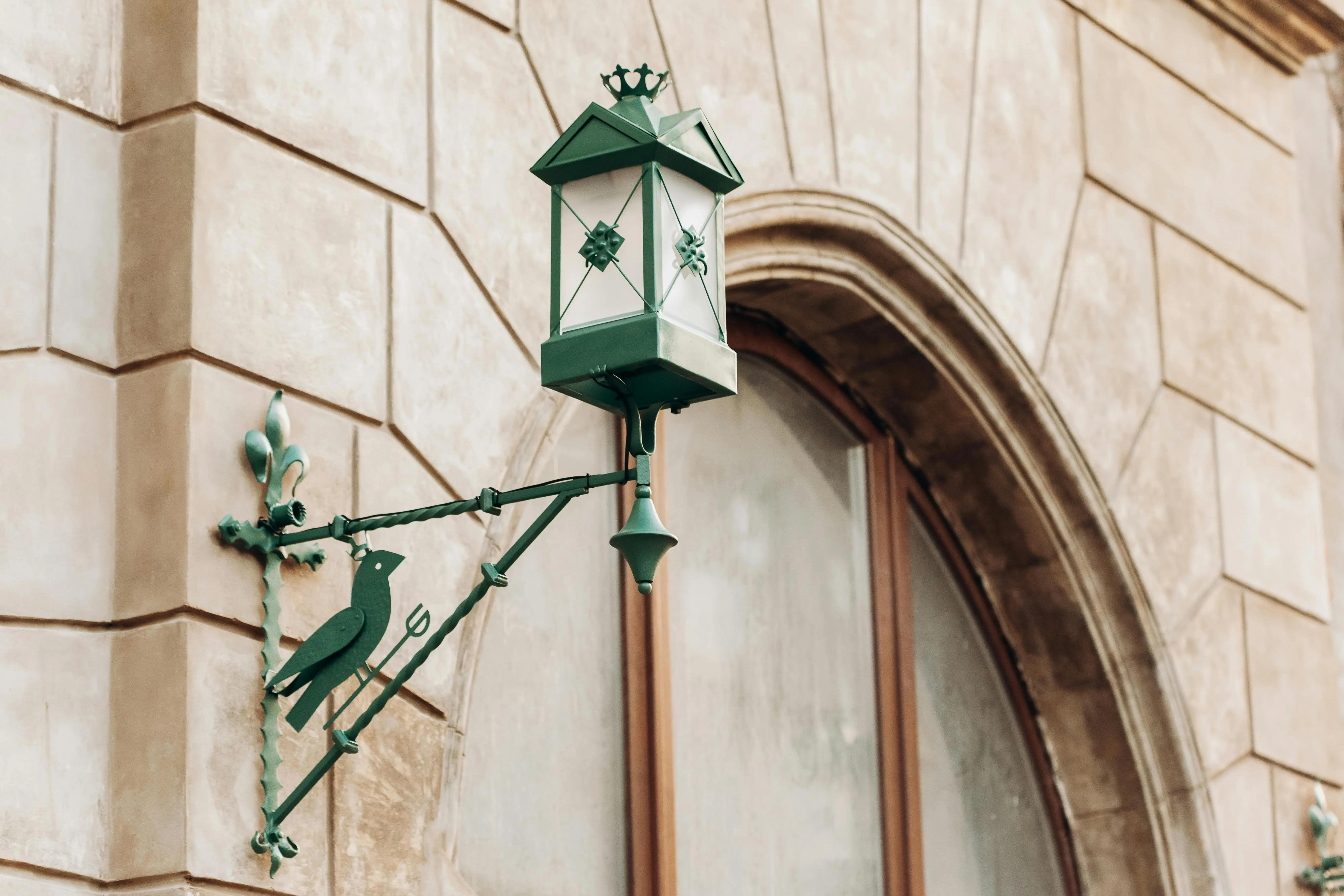 exterior wall lantern Green lantern with bird detail on a stone building facade, ideal for architectural themes.