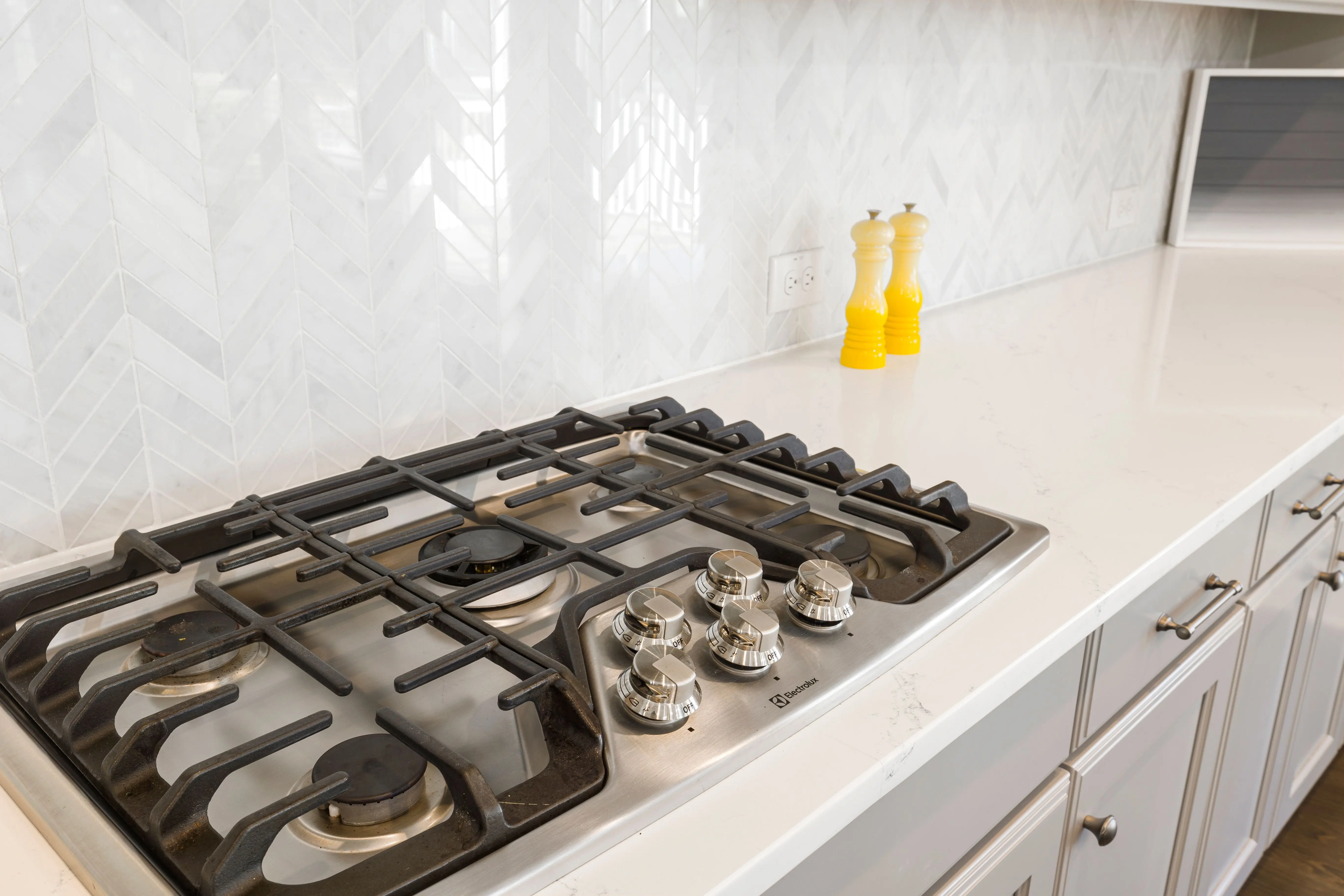 white shaker cabinet Sleek kitchen countertop featuring a gas stove and white tiled backsplash, with yellow salt and pepper shakers.