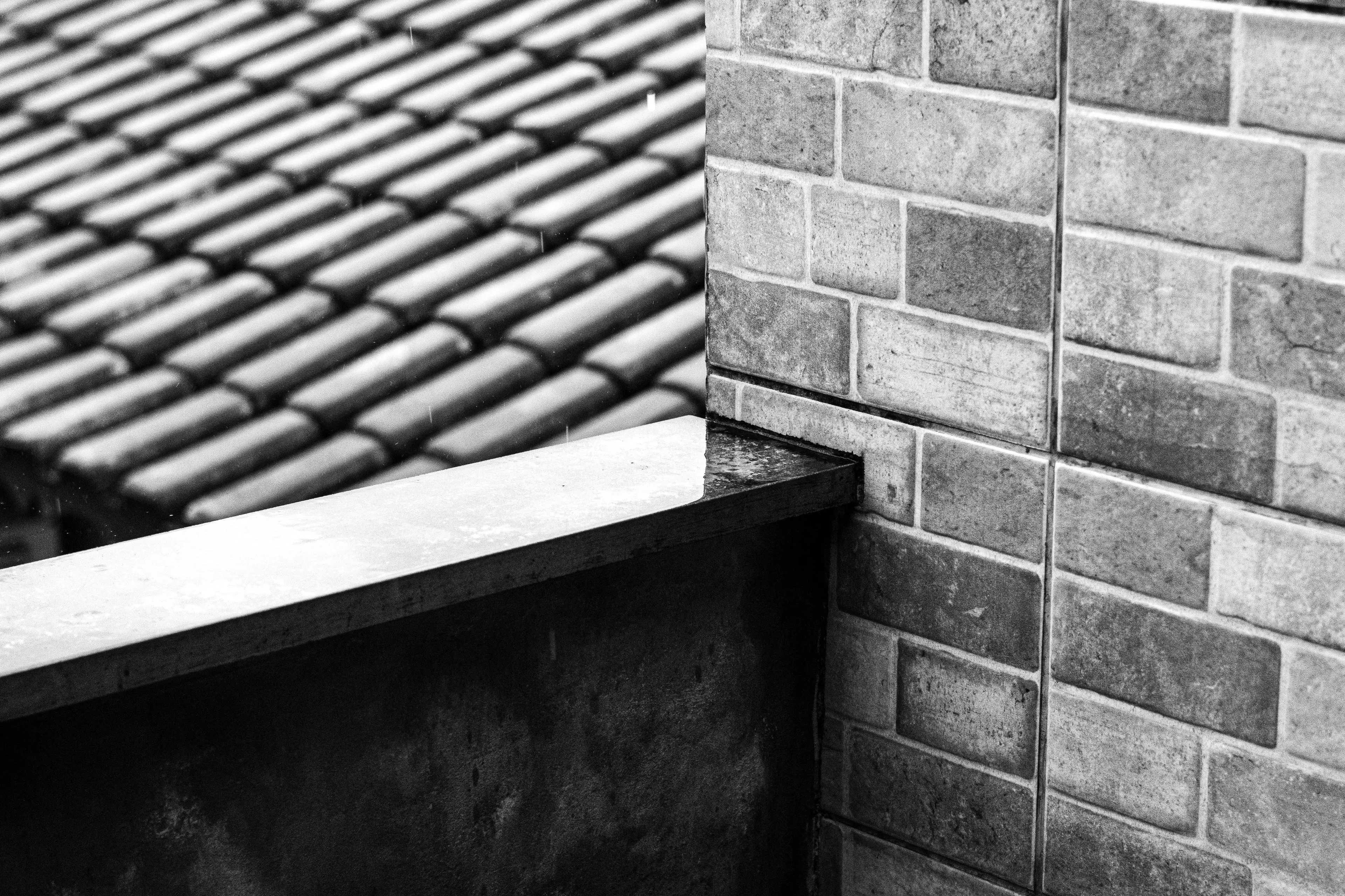 white tiles Moody black and white image of tiled roof and brick wall creating a geometric pattern.