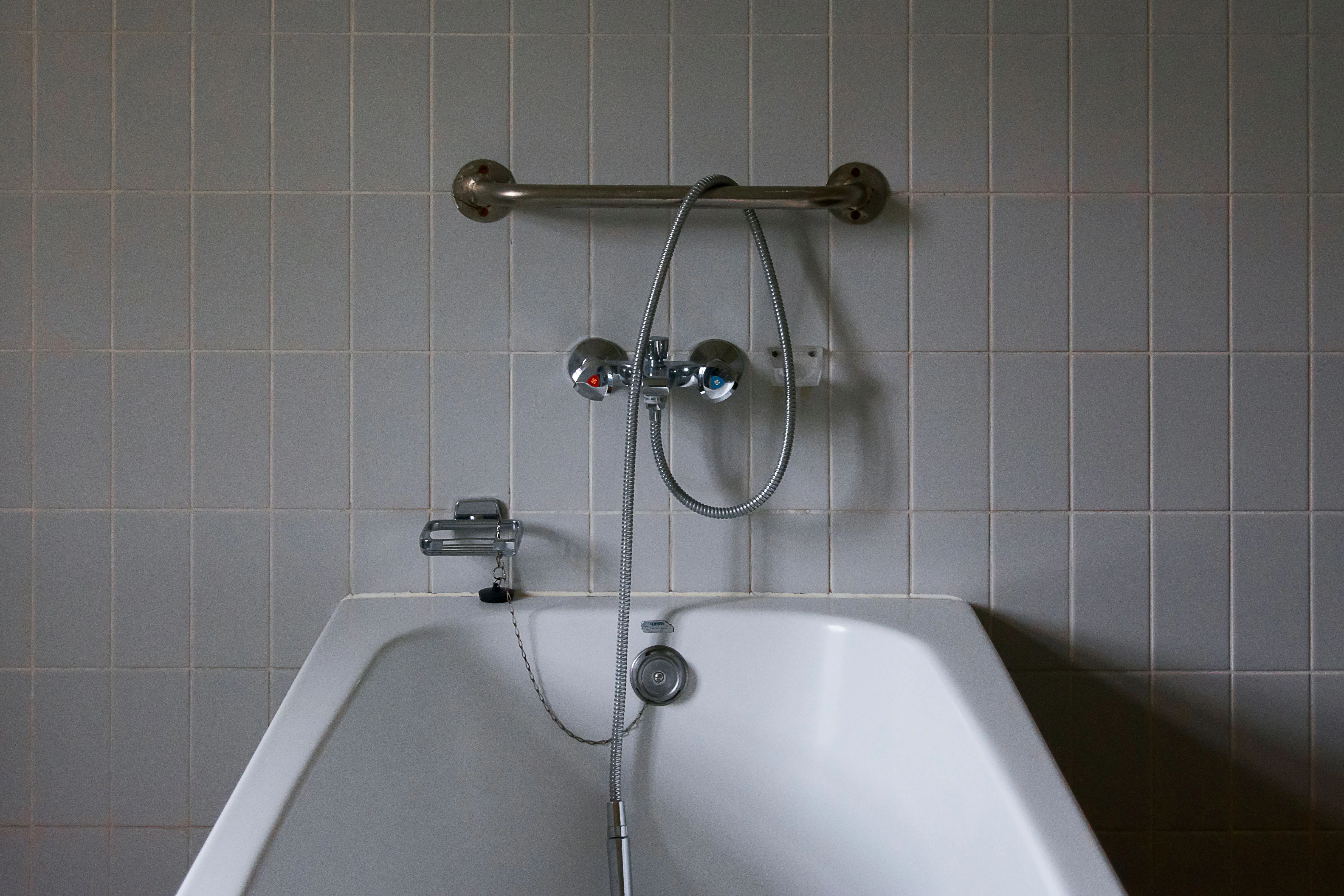 gray tile Close-up of a minimalist bathroom featuring a modern bathtub and chrome faucet against tiled walls.