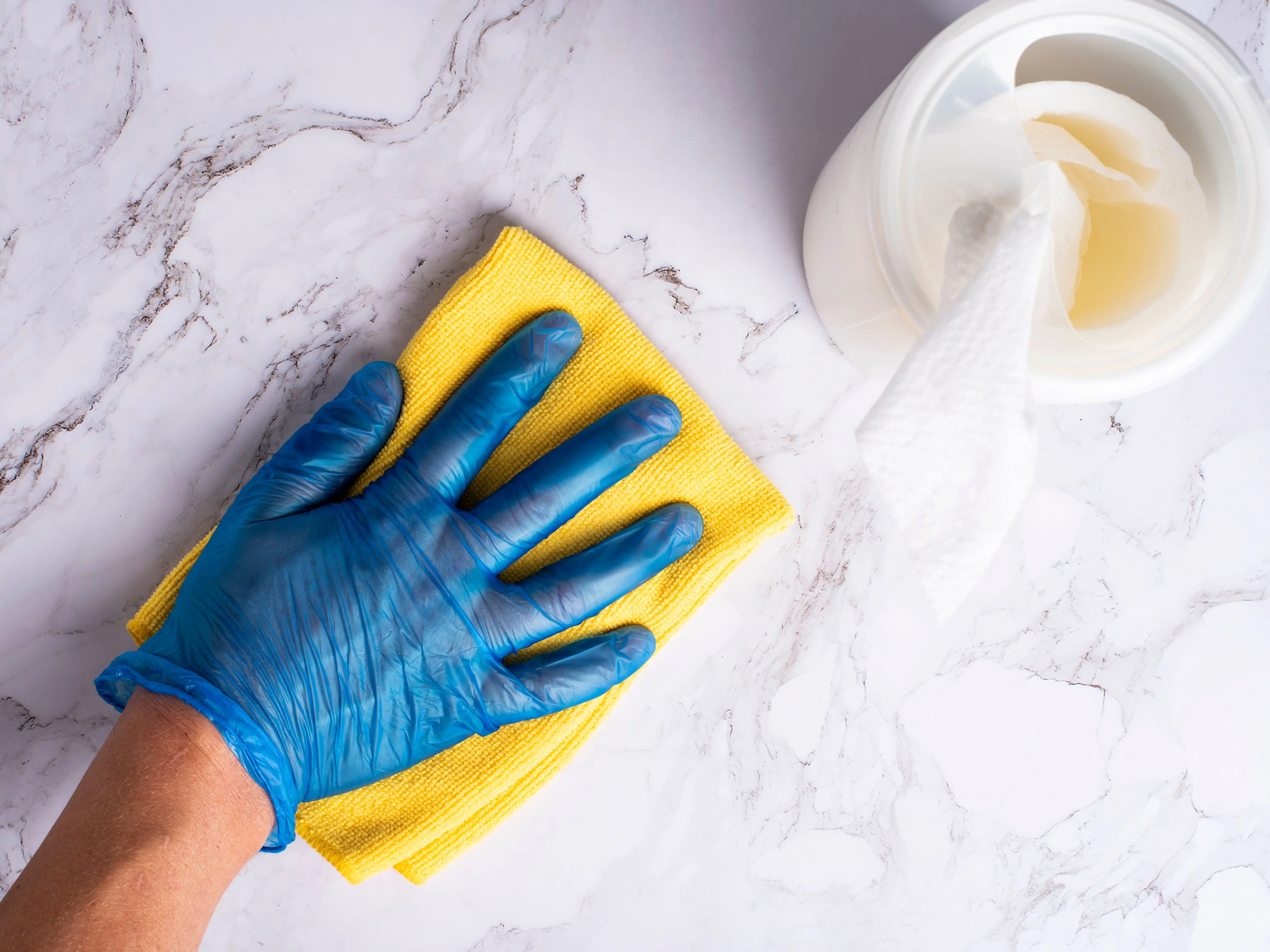 why make trims and doors satin paint A gloved hand cleans a marble countertop with a yellow cloth next to disinfectant wipes.