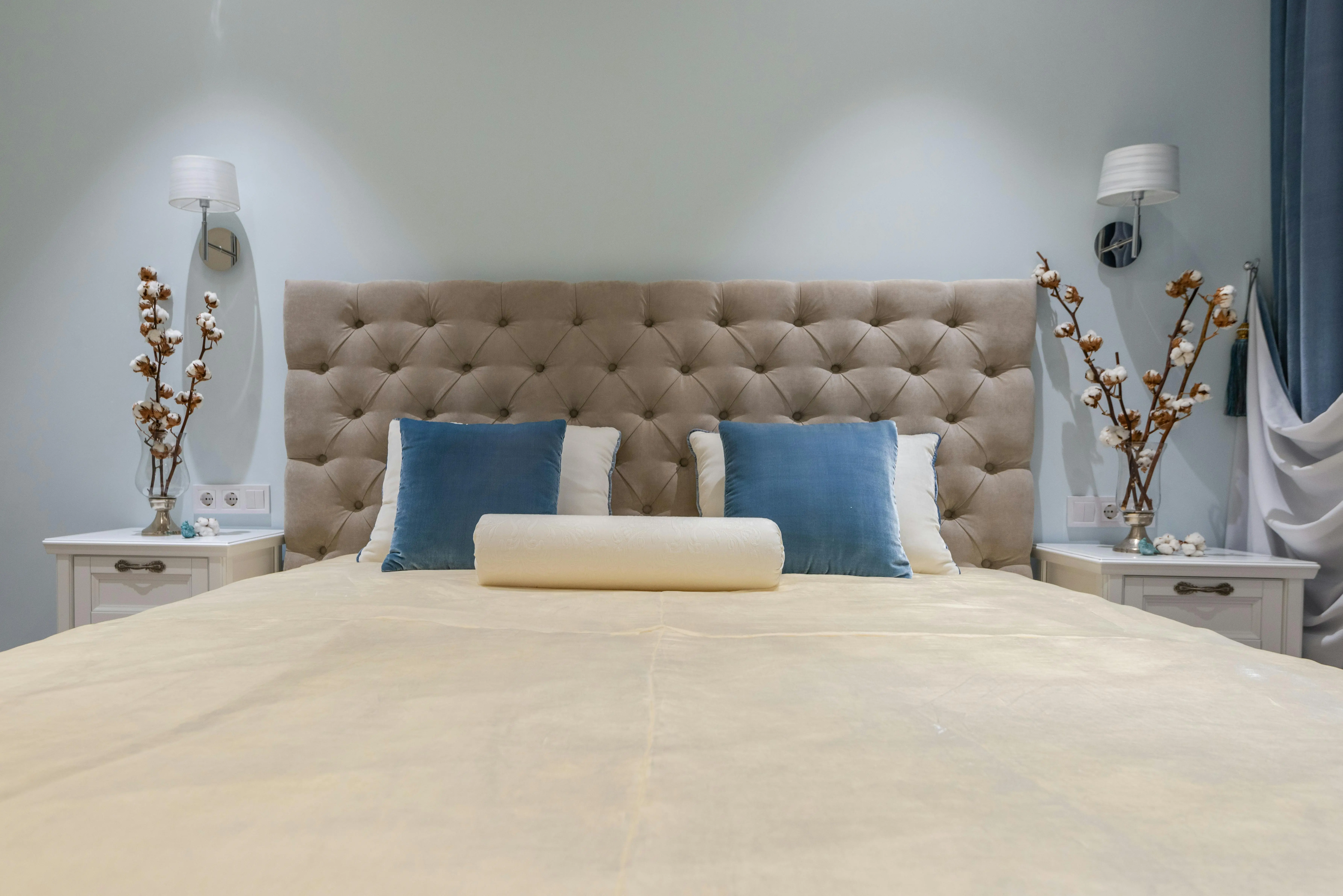 blue accent pillows Comfortable bed with pillows and nightstands decorated with blooming flowers in cozy classic styled bedroom