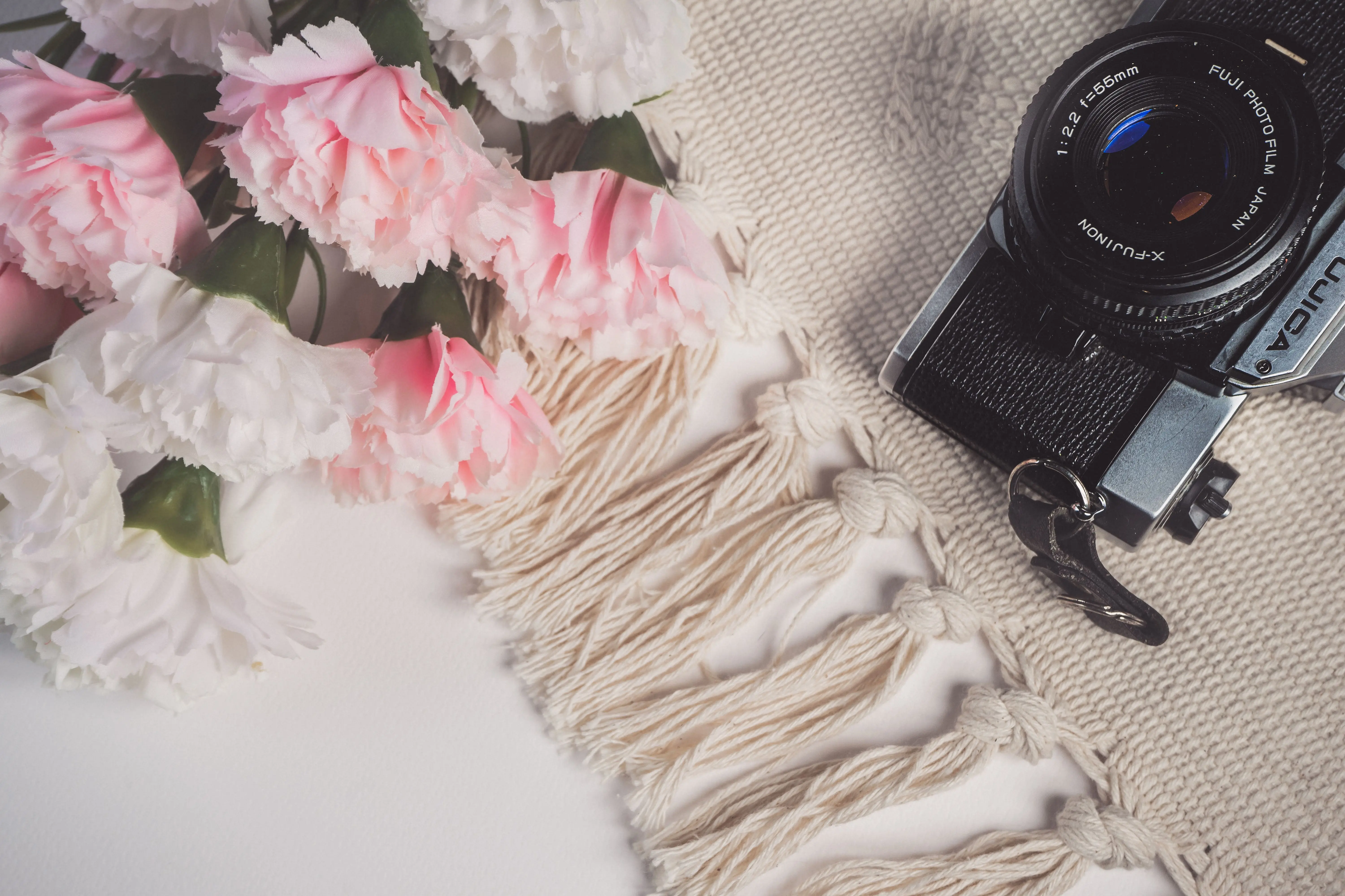 boho comforter set A vintage analog camera beside pink and white carnations on a textured fabric background.