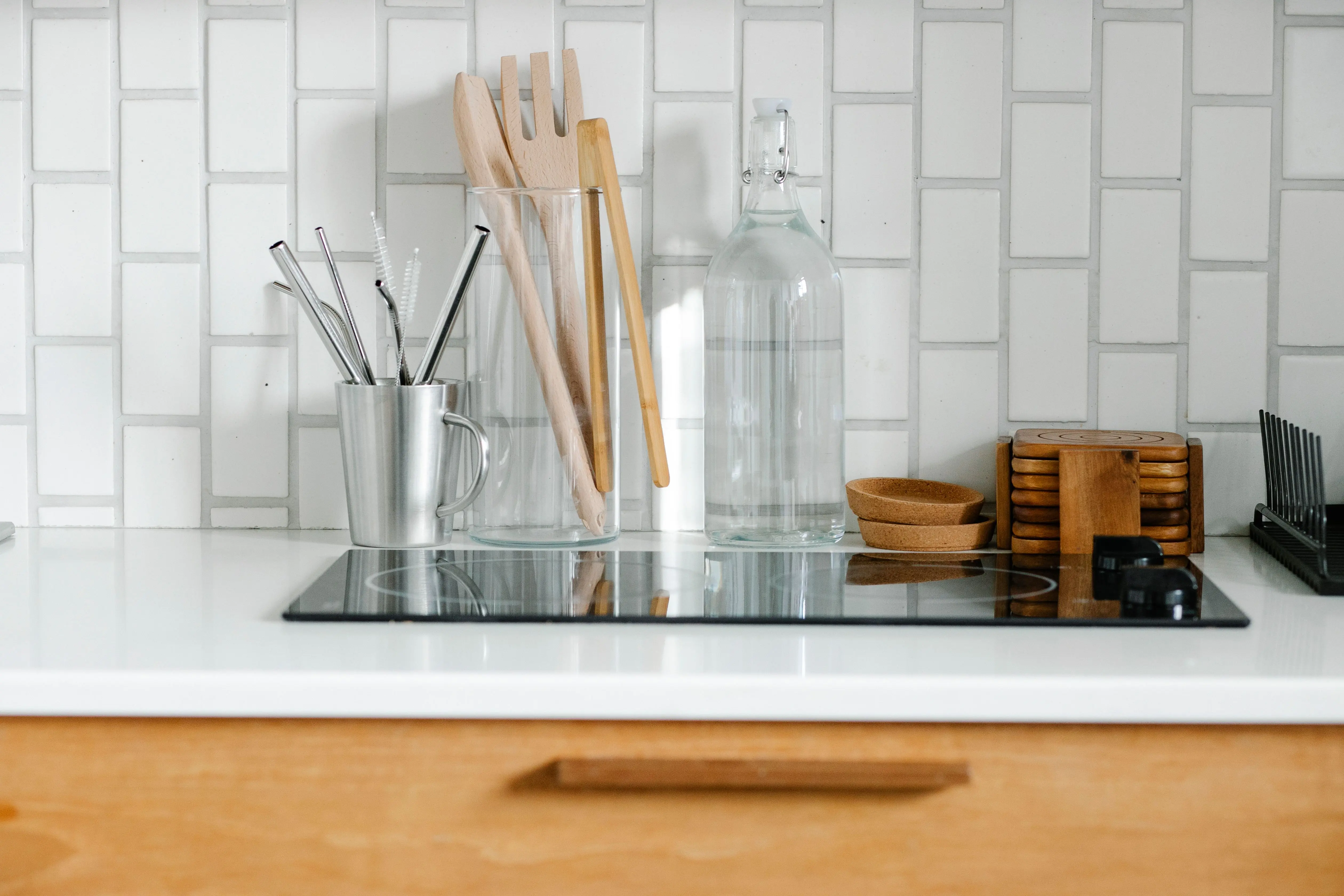 white kitchen backsplash A modern minimalist kitchen counter featuring utensils, glass bottles, and a ceramic backsplash.
