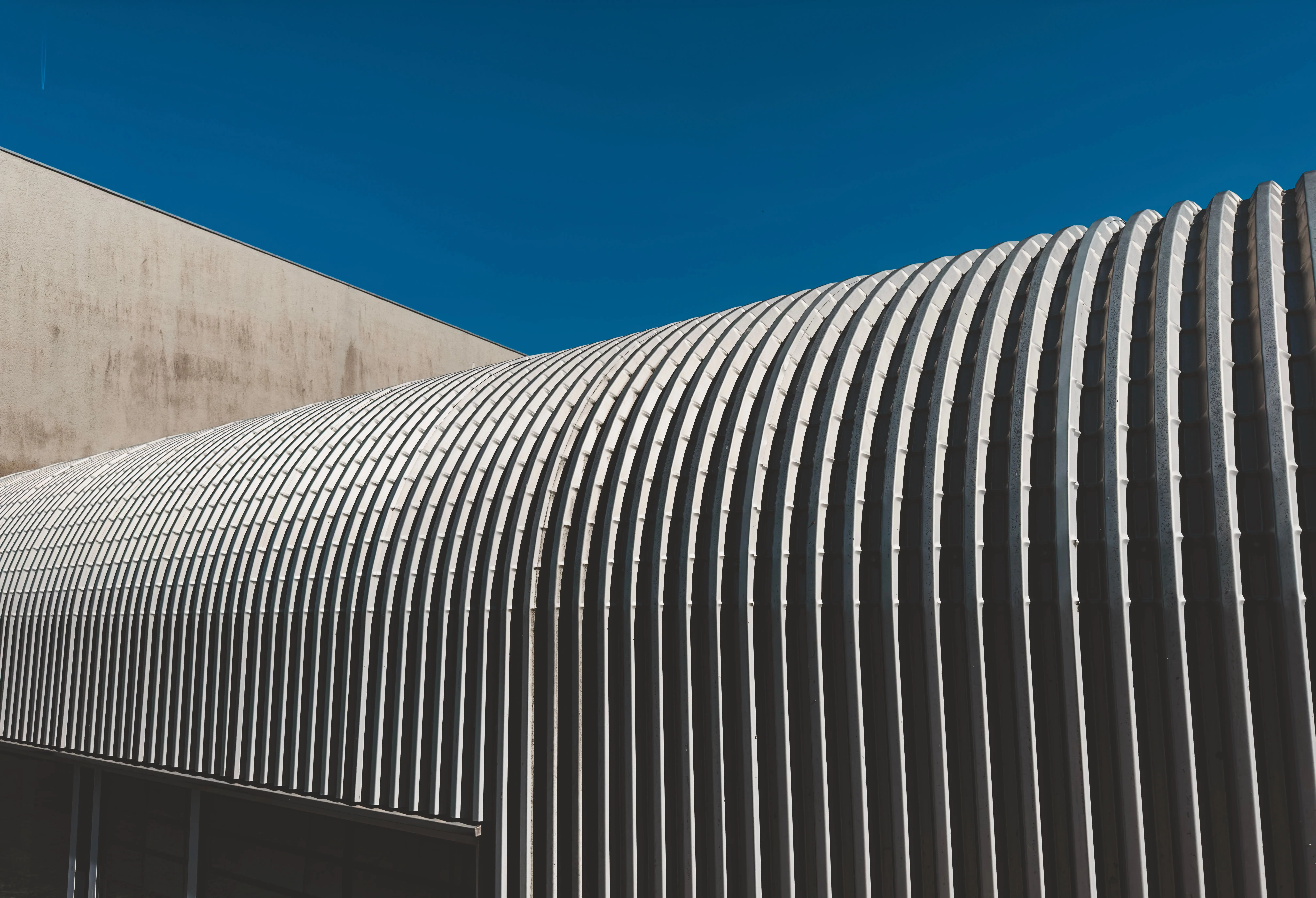 steel roof coating A sleek and modern corrugated metal facade with repeating stripes against a clear blue sky.
