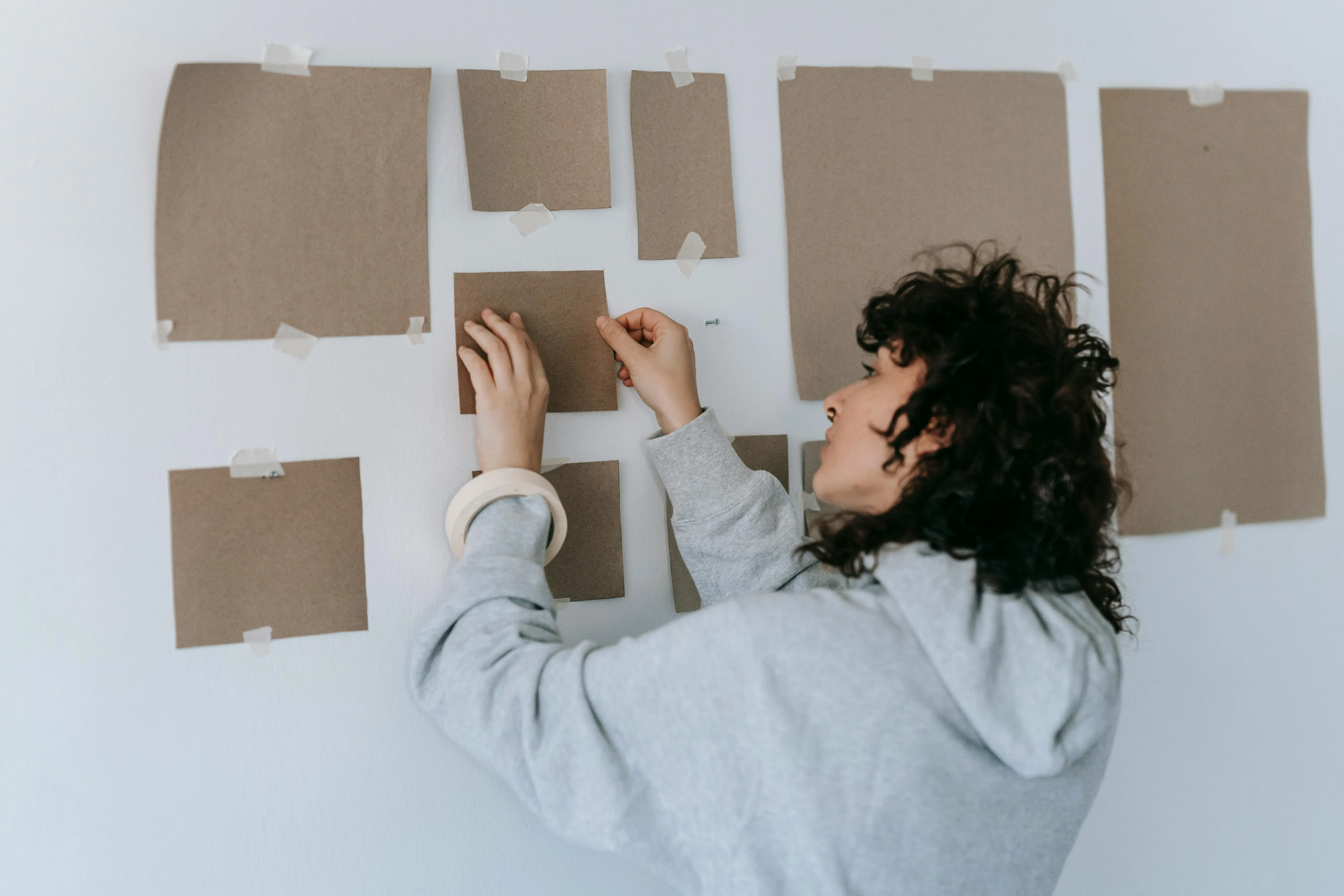 colorful art A woman in casual attire arranges cardboard pieces on a wall during an indoor art project.