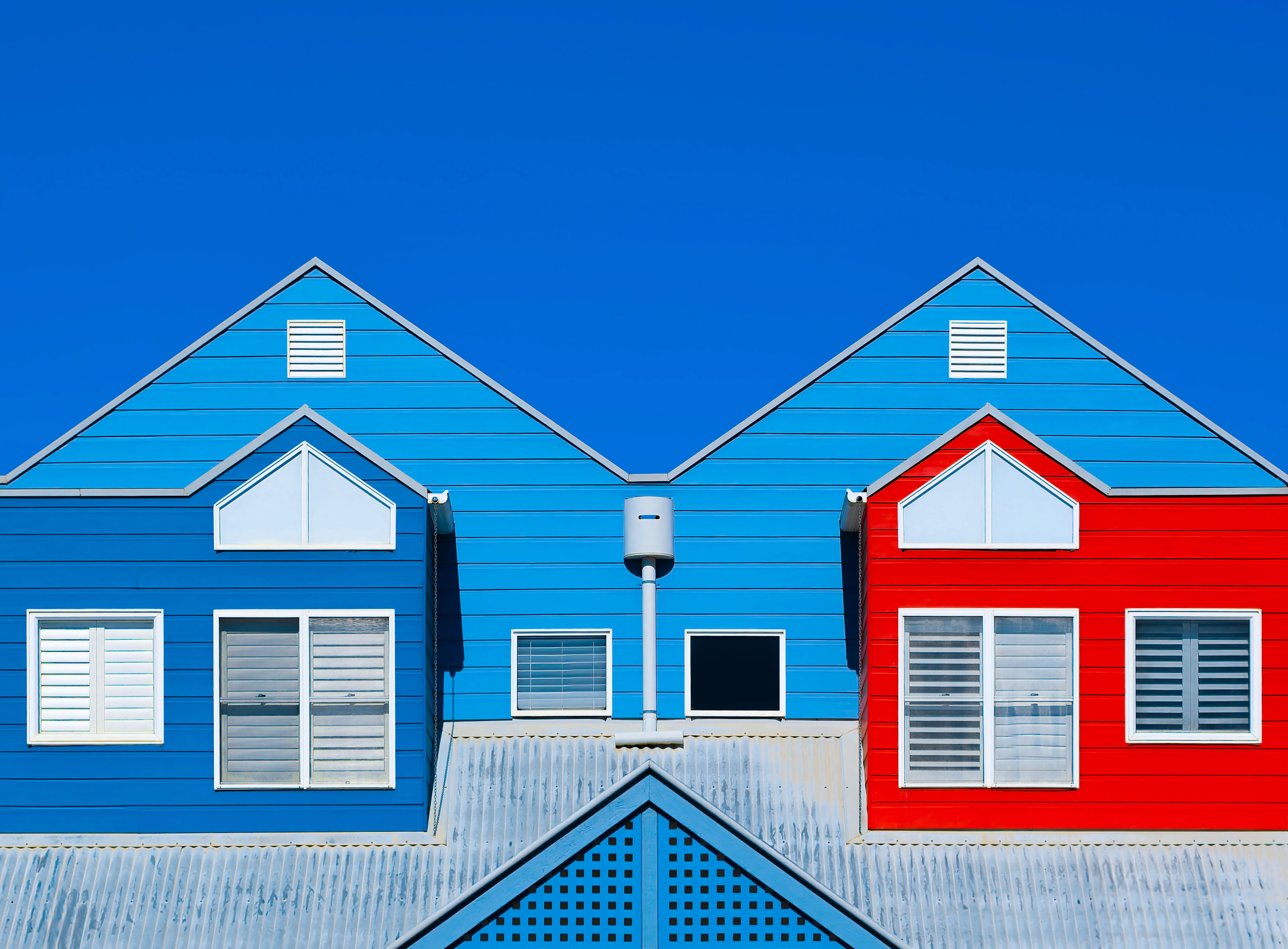 painting cost per square foot Brightly painted house facades in blue and red create a striking contrast against a clear blue sky.