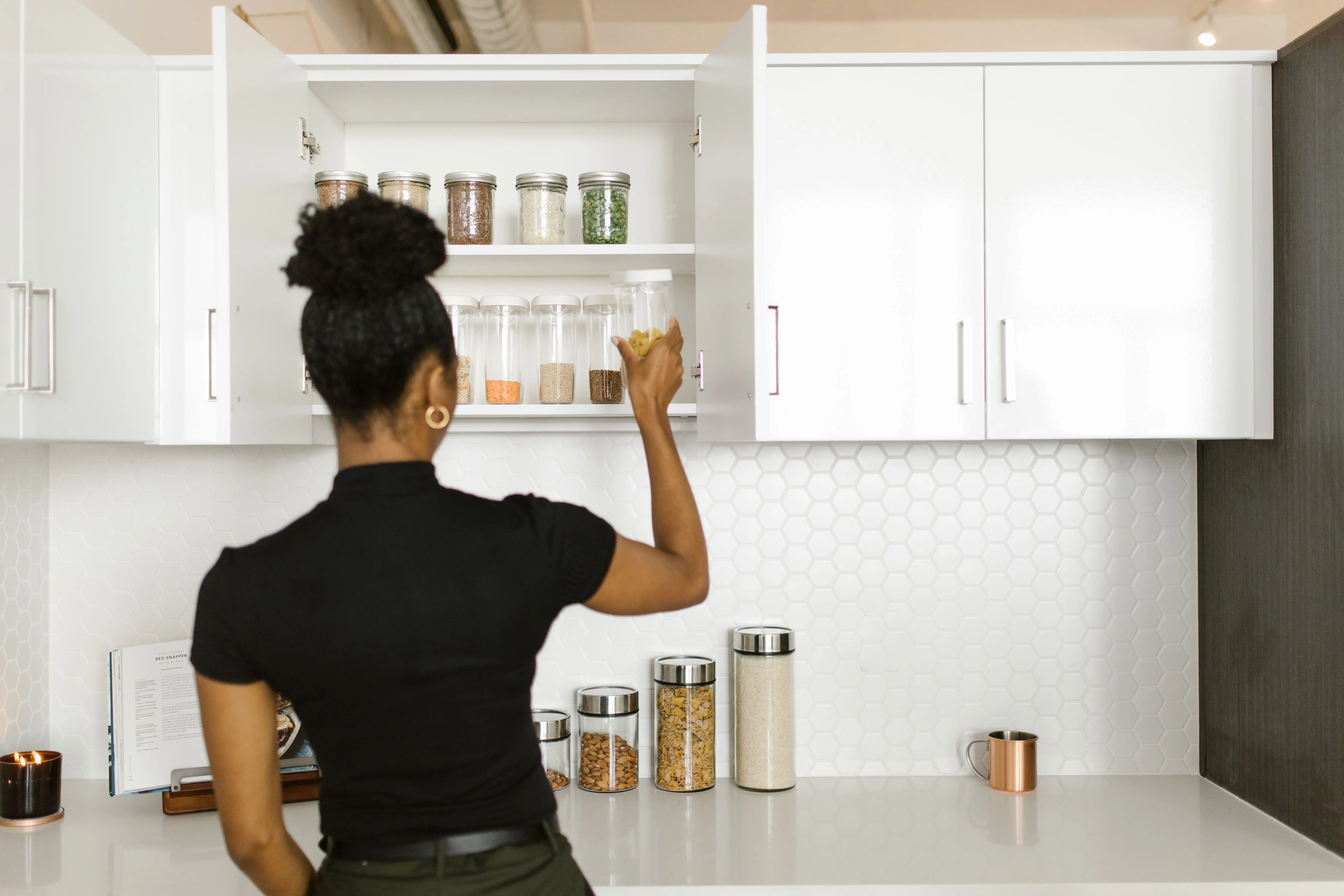 kitchen cabinet with drawers A woman organizing a pantry shelf with various food jars in a modern kitchen.