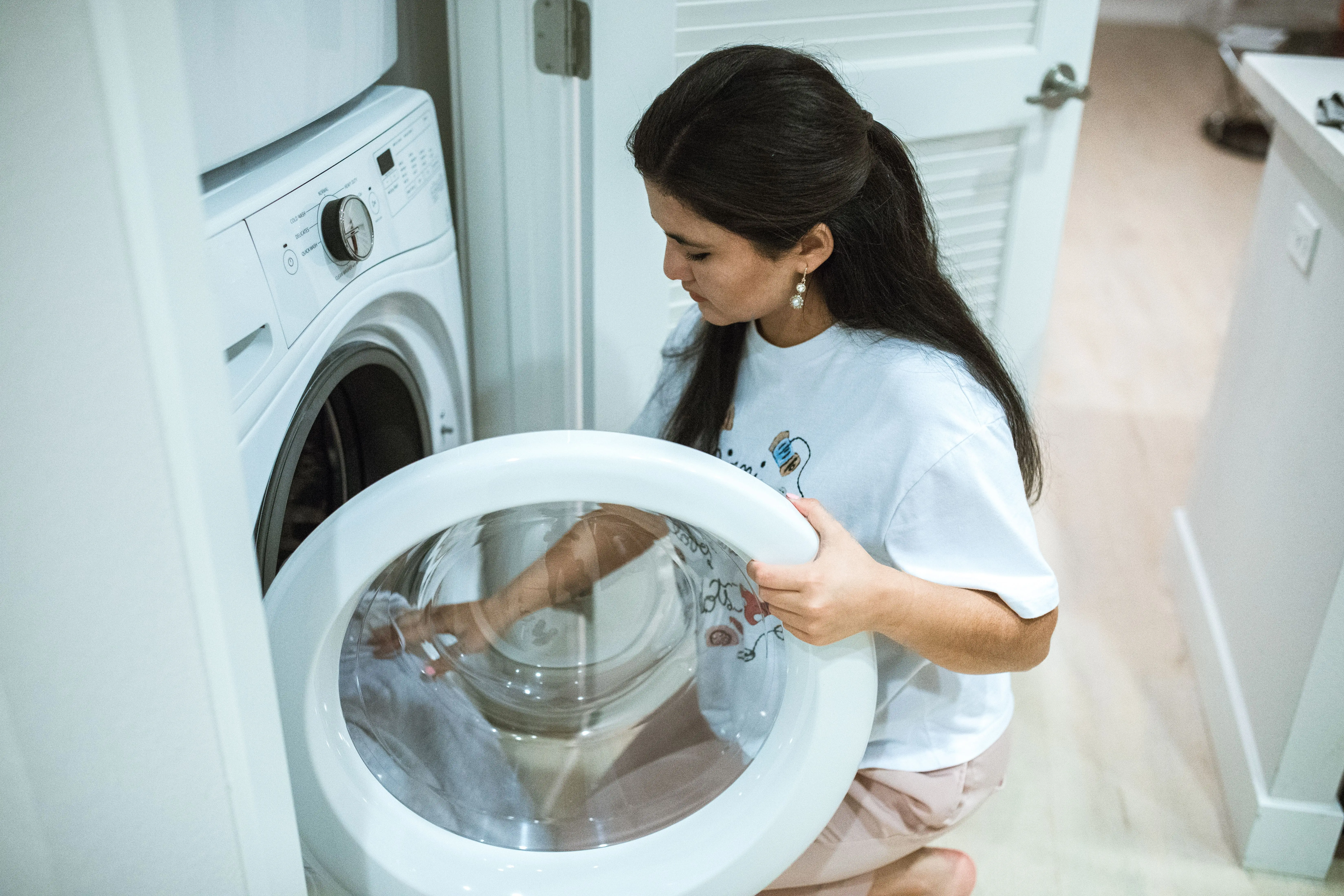 heavy duty washer A woman kneeling to load clothes into a front-loading washing machine in a modern home laundry room.
