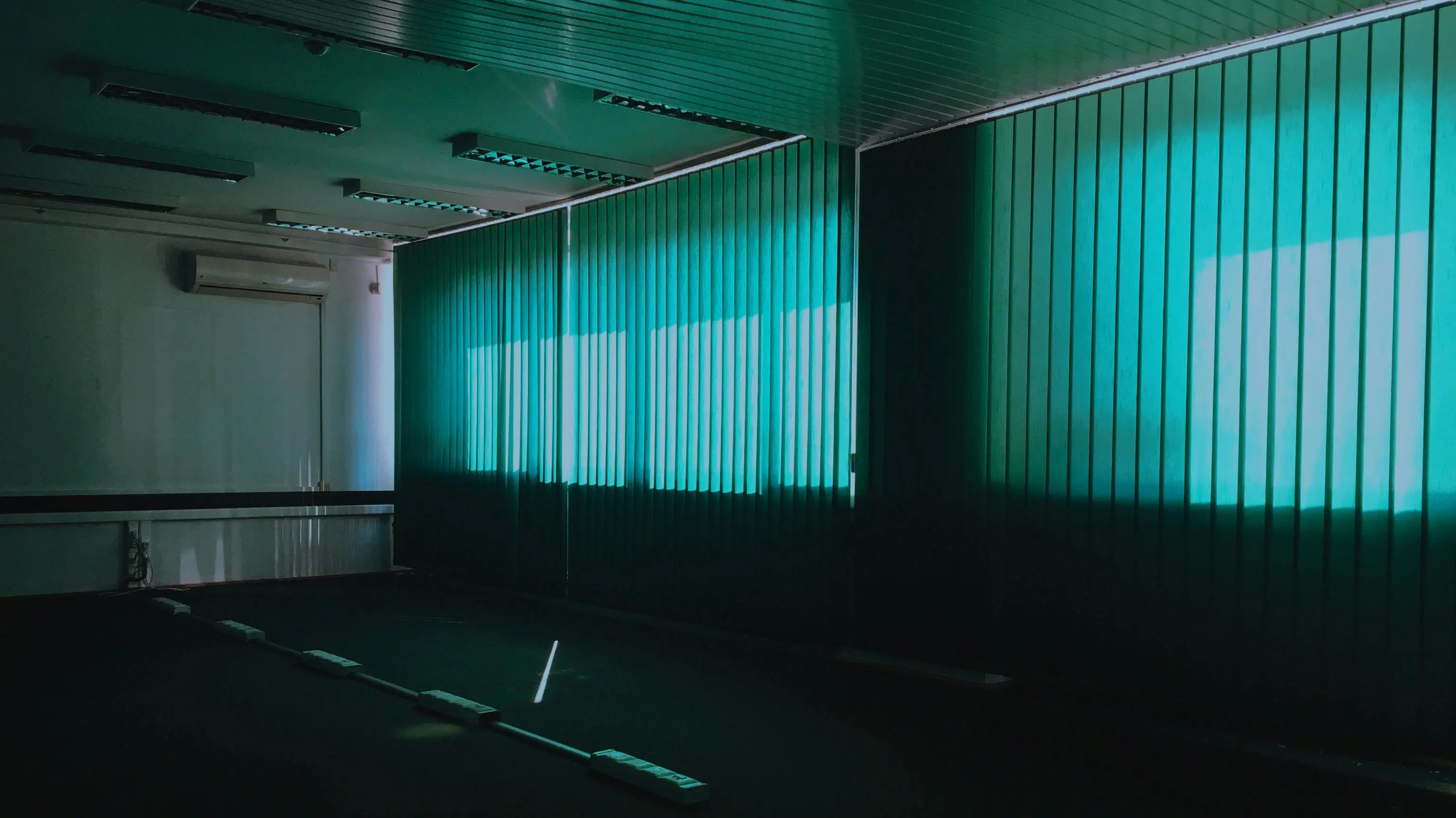 light green paint Dark empty room with vertical green blinds and natural light filtering through.