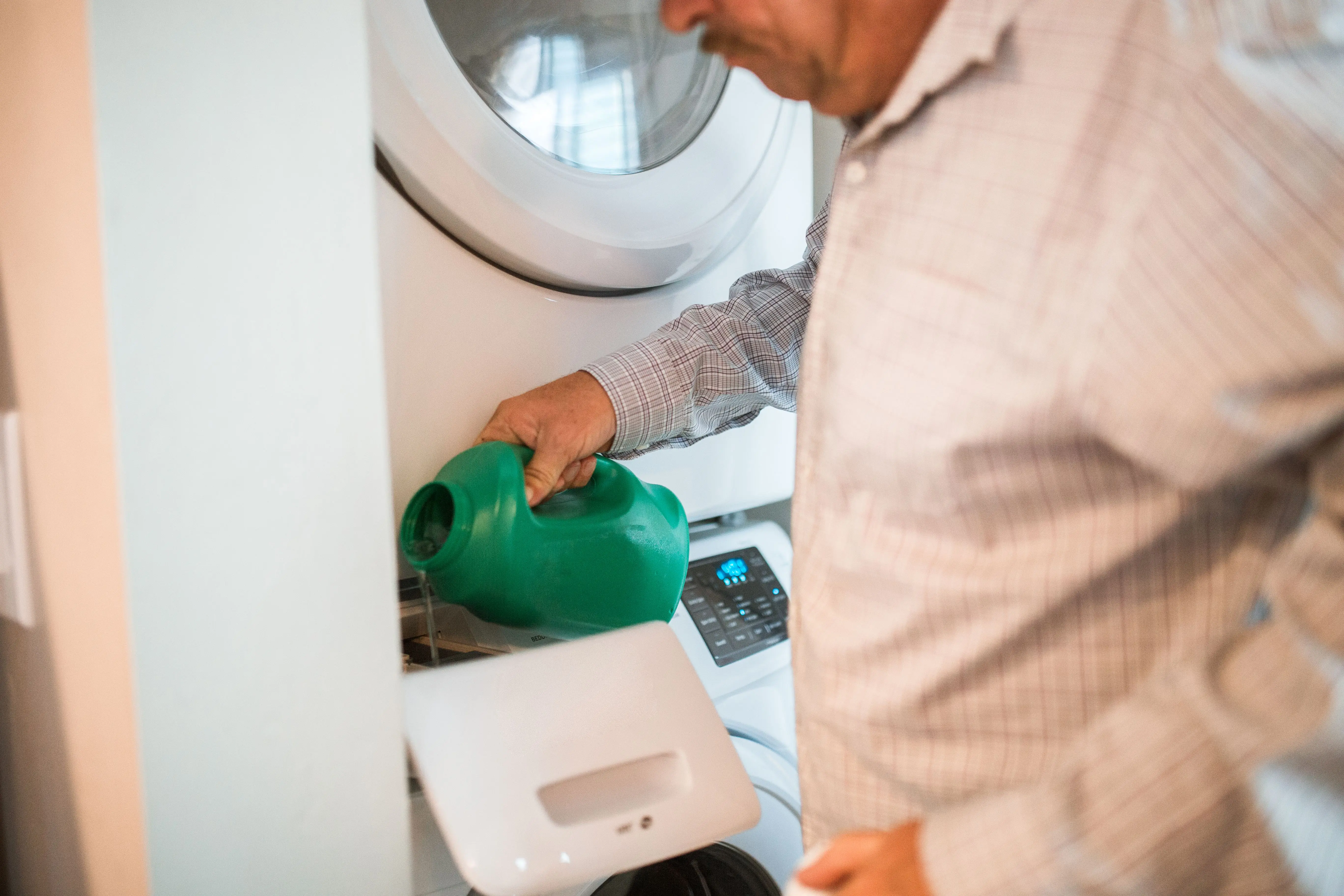 laundry detergent recipe An adult man pours detergent into a washing machine for doing laundry indoors.