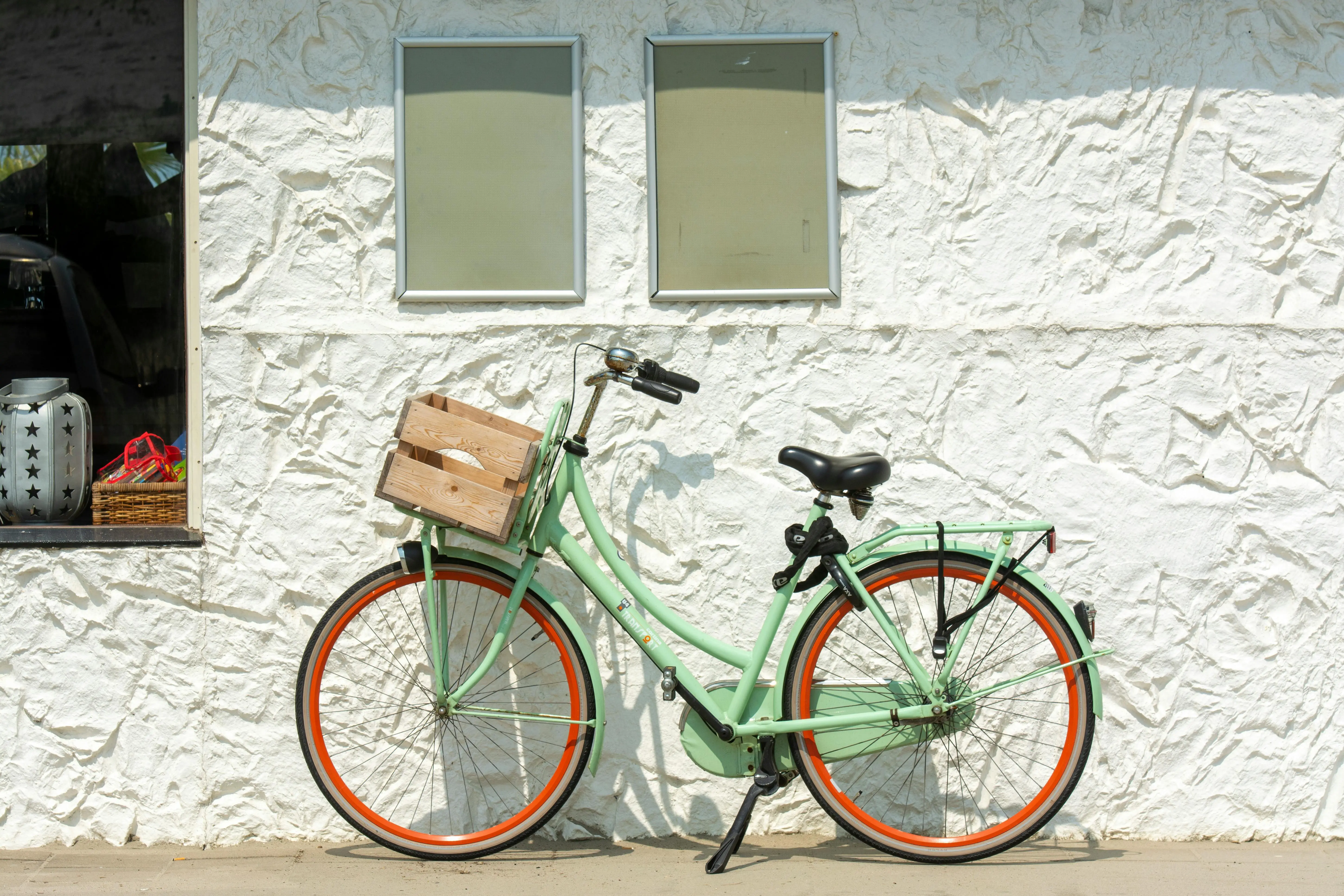 light green paint A stylish mint green bicycle with an orange rim parked against a textured white wall in sunlight.