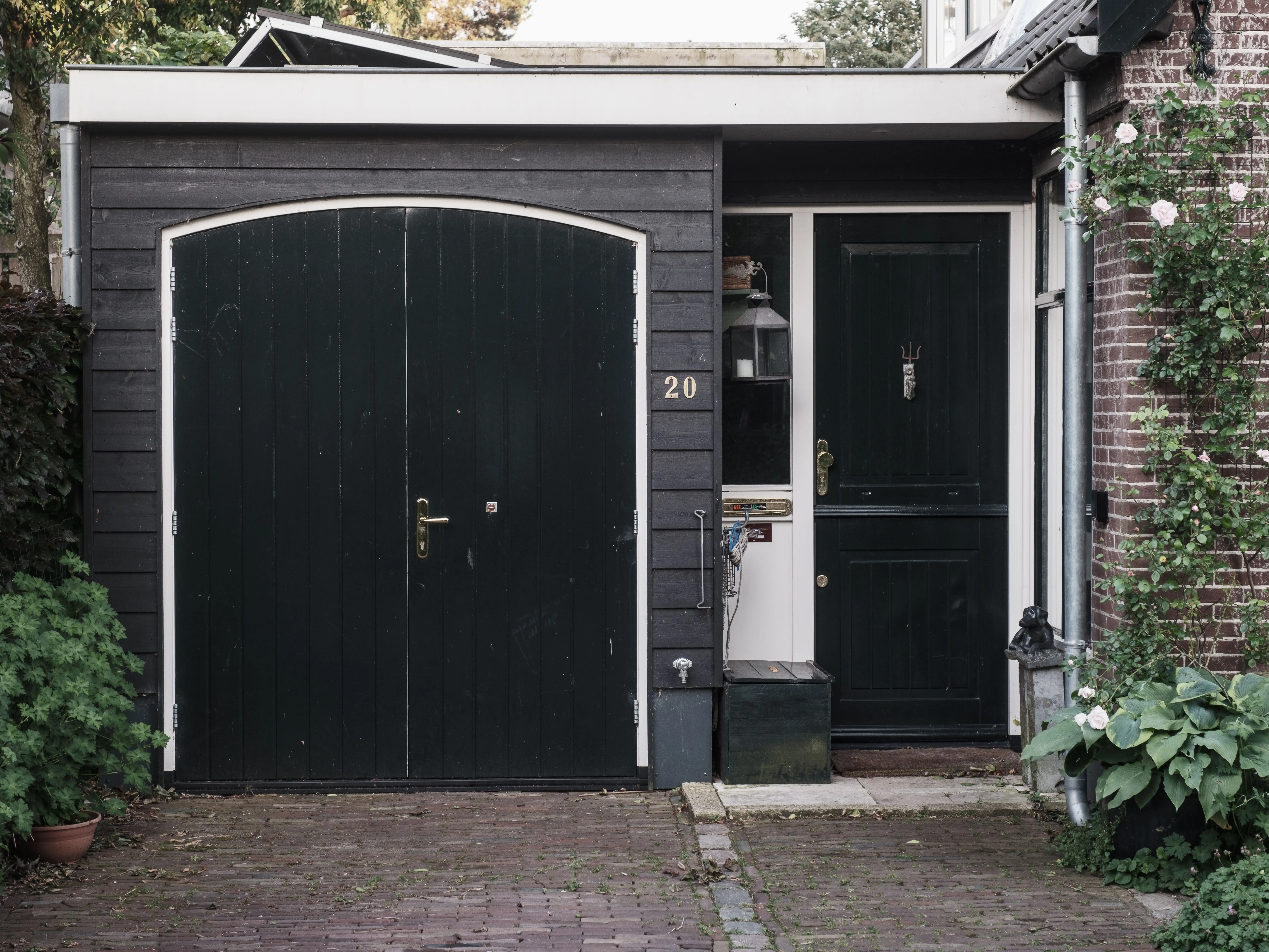 black garage door Exterior of a traditional Dutch house with black doors and a landscaped garden.