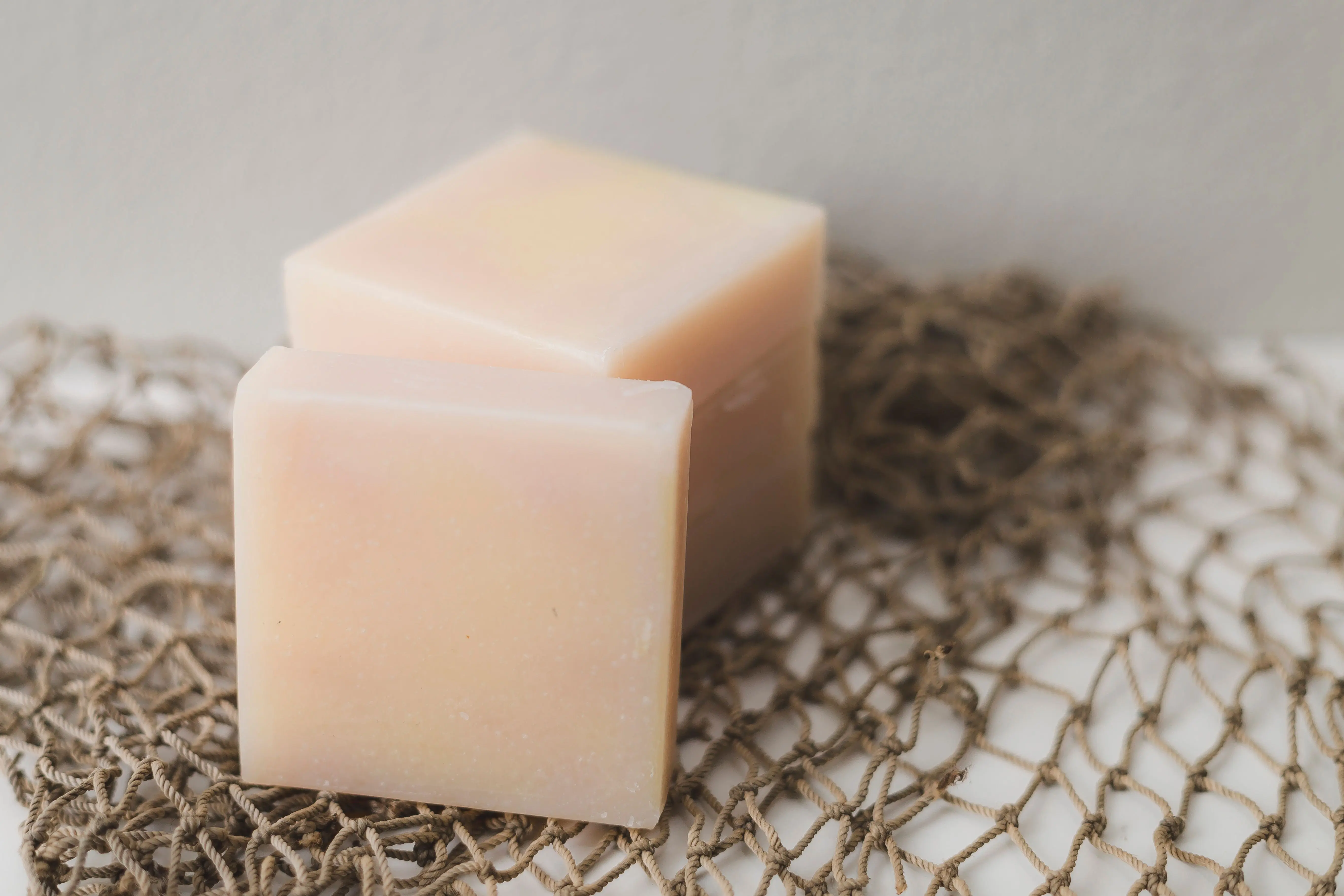 laundry detergent recipe Two bars of natural handmade soap placed on a rustic netting backdrop, perfect for a spa theme.