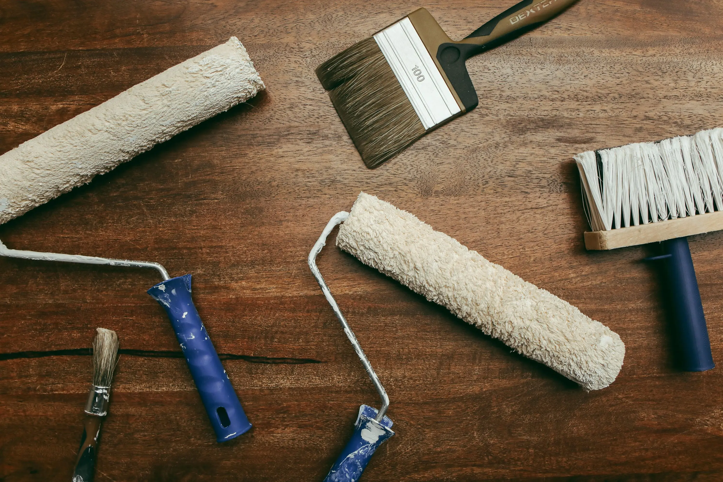 painting cost per square foot Top view of various painting tools including rollers and brushes laid out on a wooden surface.