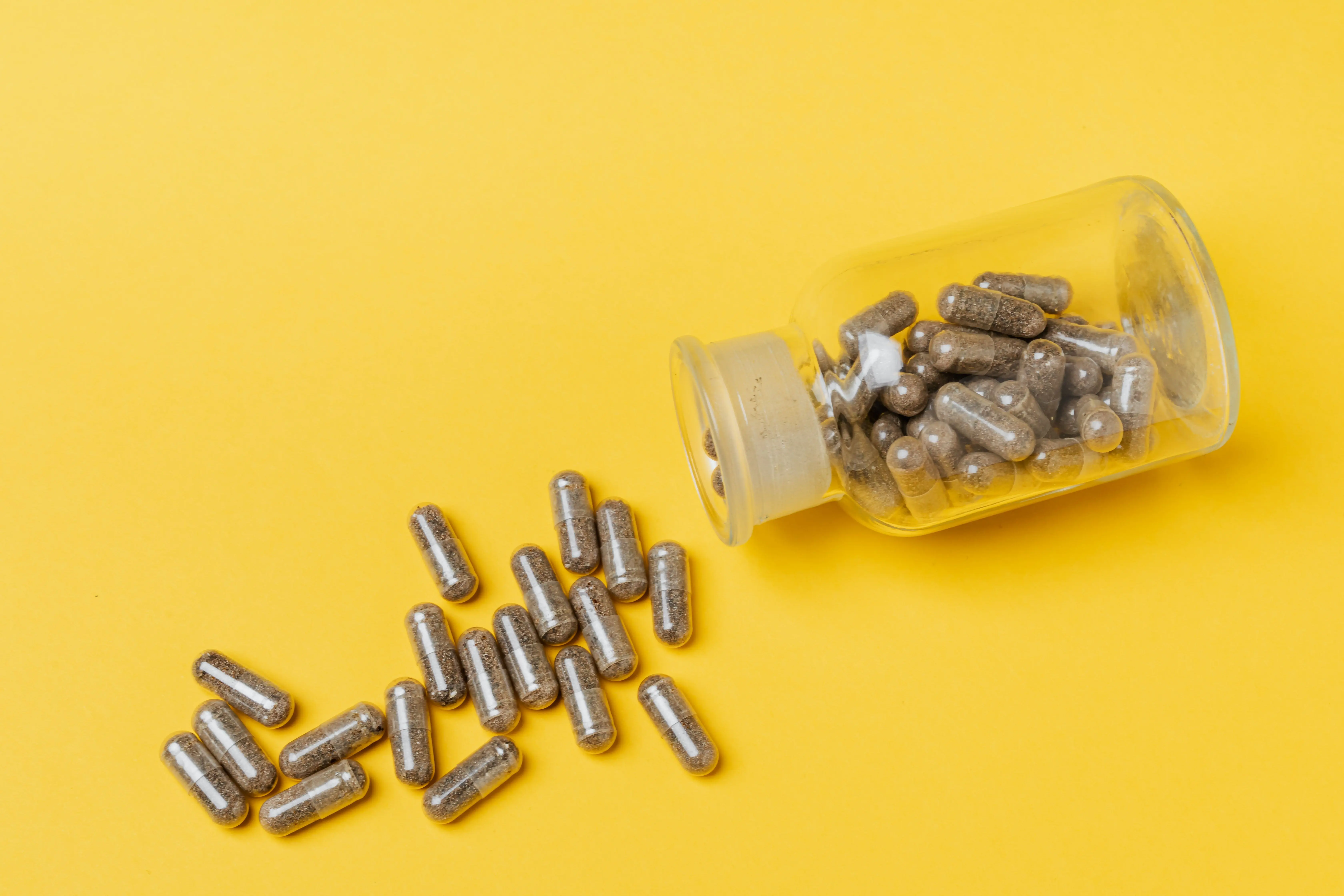 parrot food A glass bottle spilling capsules on a vivid yellow background. Perfect for healthcare and medicine themes.