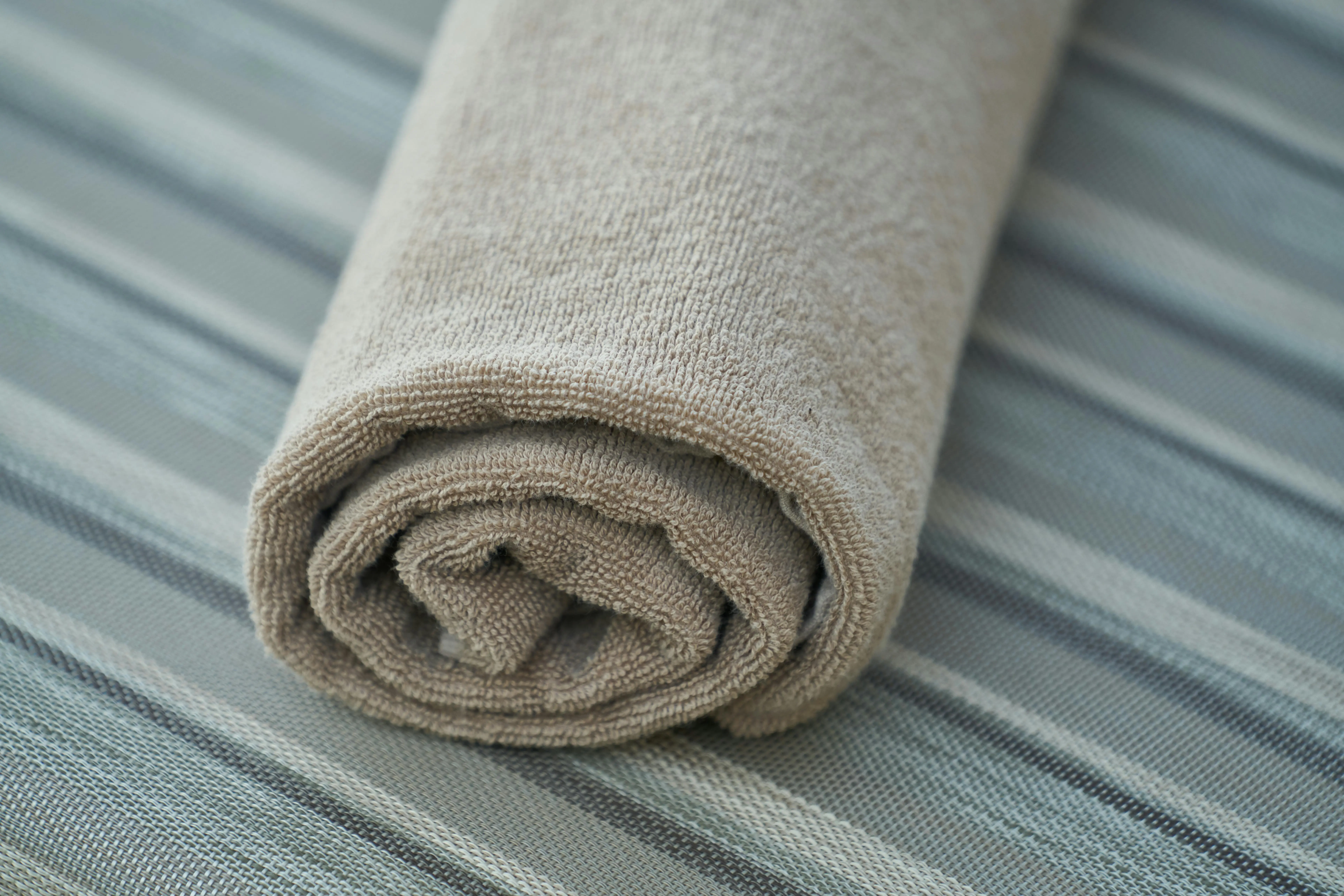 bathroom wall accessories Close-up of a soft beige cotton towel rolled neatly on a striped fabric surface. Perfect for home decor or textile themes.