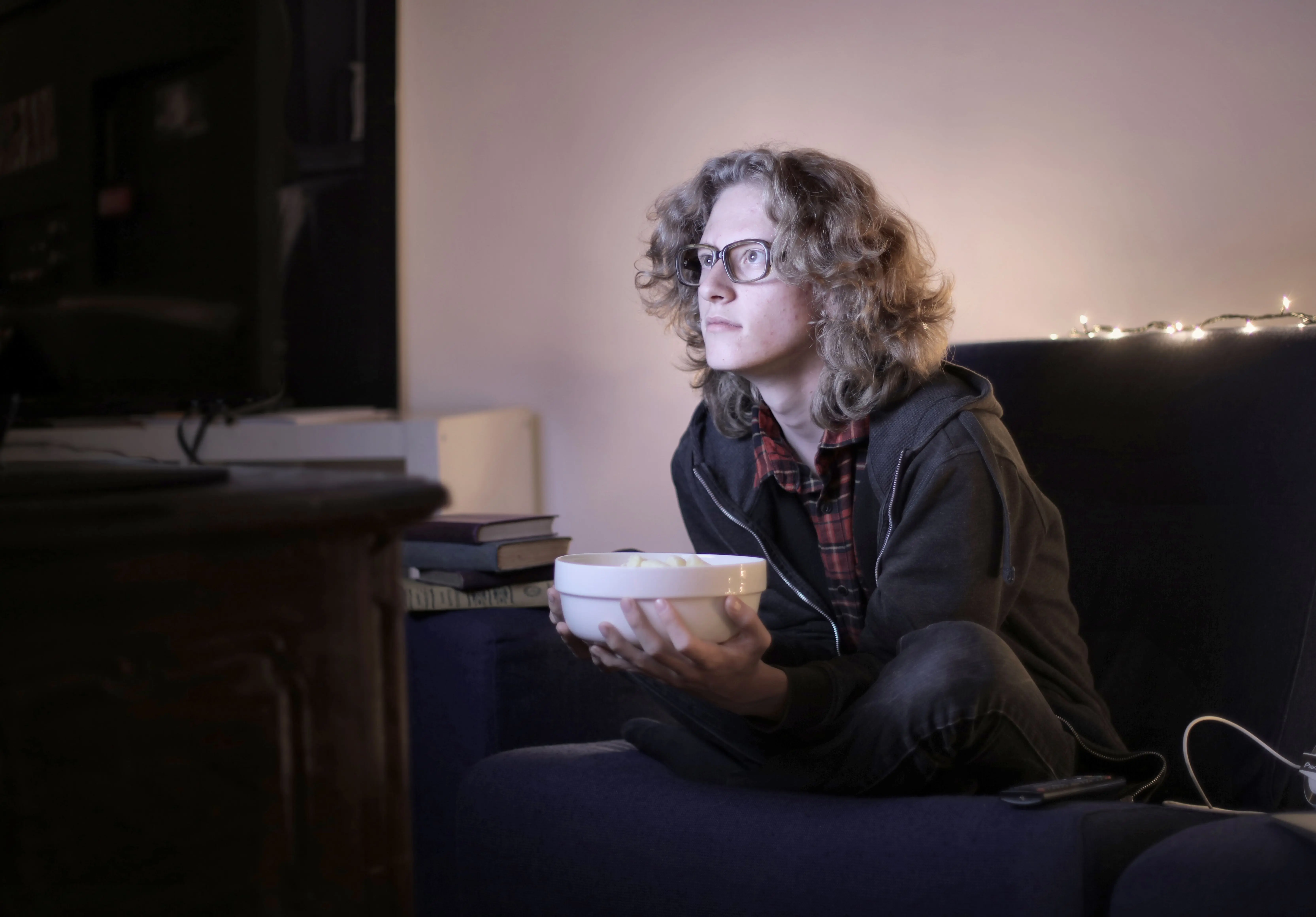 small living room ideas with tv Concentrated male teenage with long hair in casual wear and eyeglasses sitting on couch with bowl of popcorn and watching interesting movie while resting in cozy living room at home