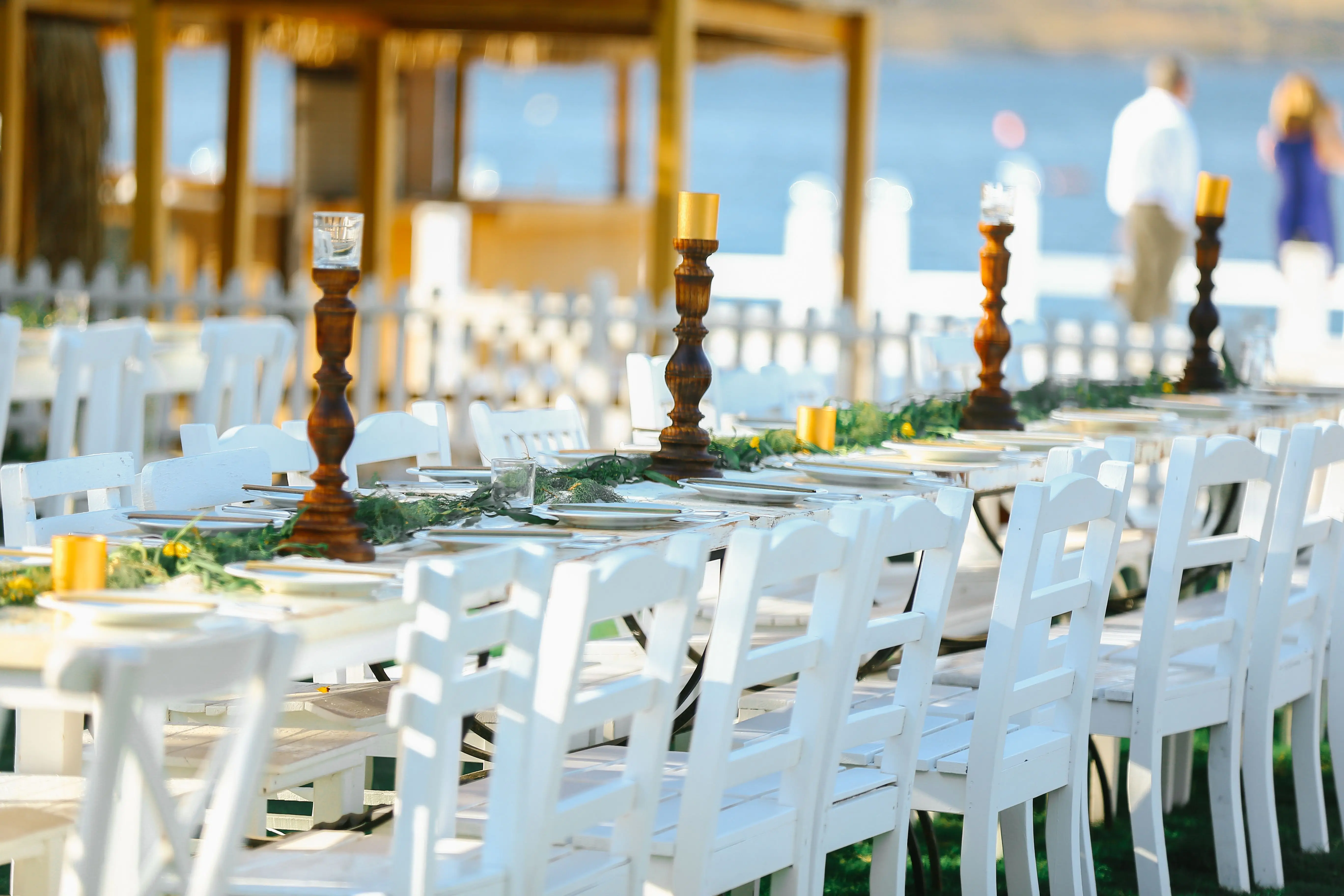 tall candle holders Beautiful outdoor wedding reception with white chairs and decorated tables by the seaside.