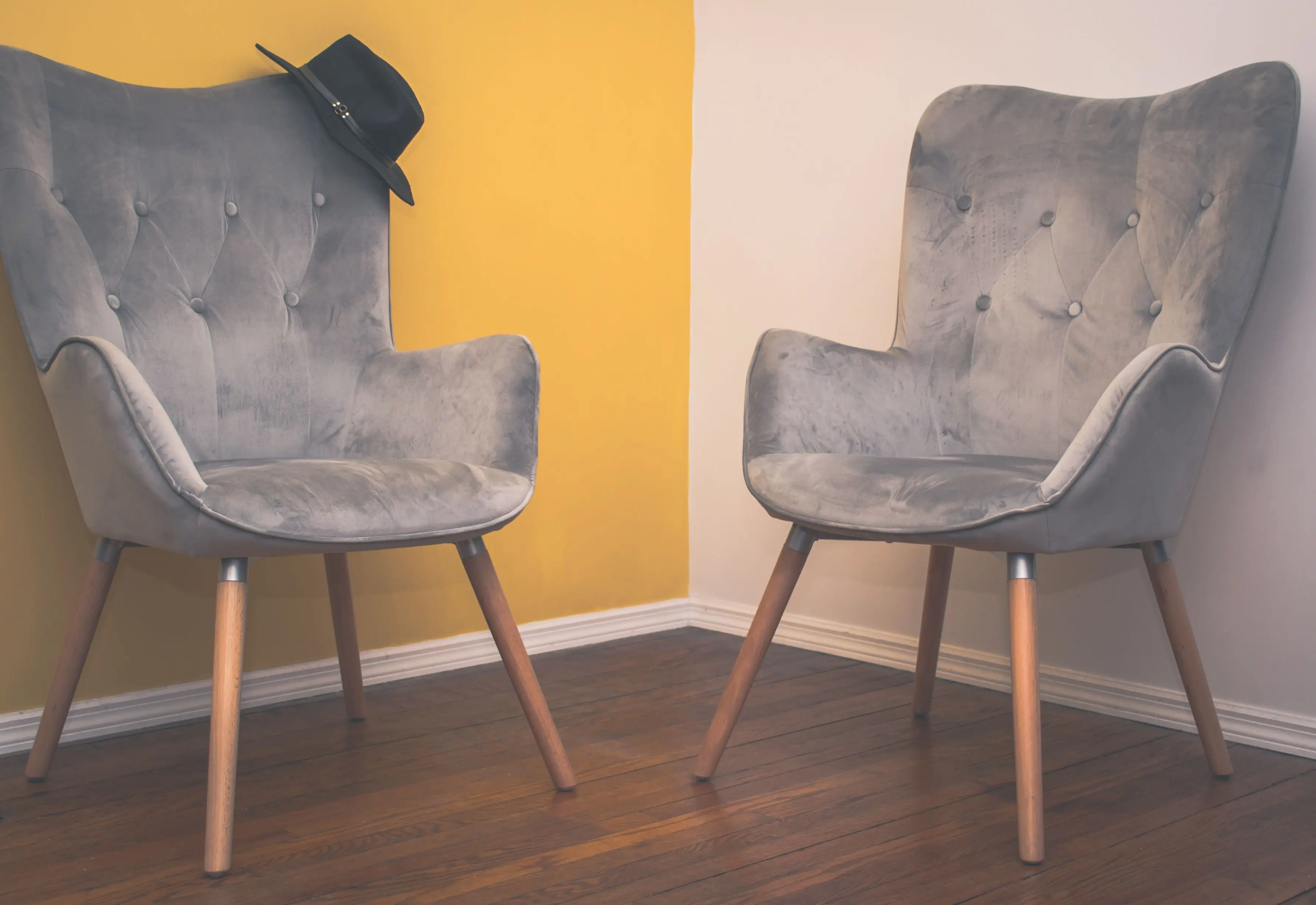 living room chairs set of 2 Two contemporary gray armchairs in a minimalist interior with a yellow accent wall and wooden flooring.