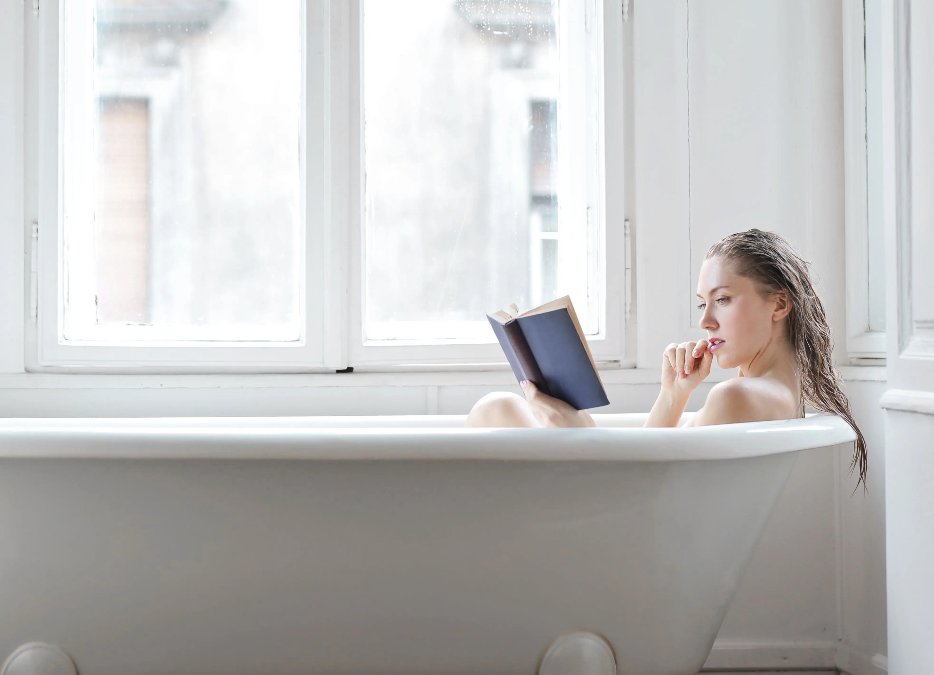 homemade laundry soap Woman reading a book while relaxing in a bathtub by a window, enjoying a quiet moment indoors.