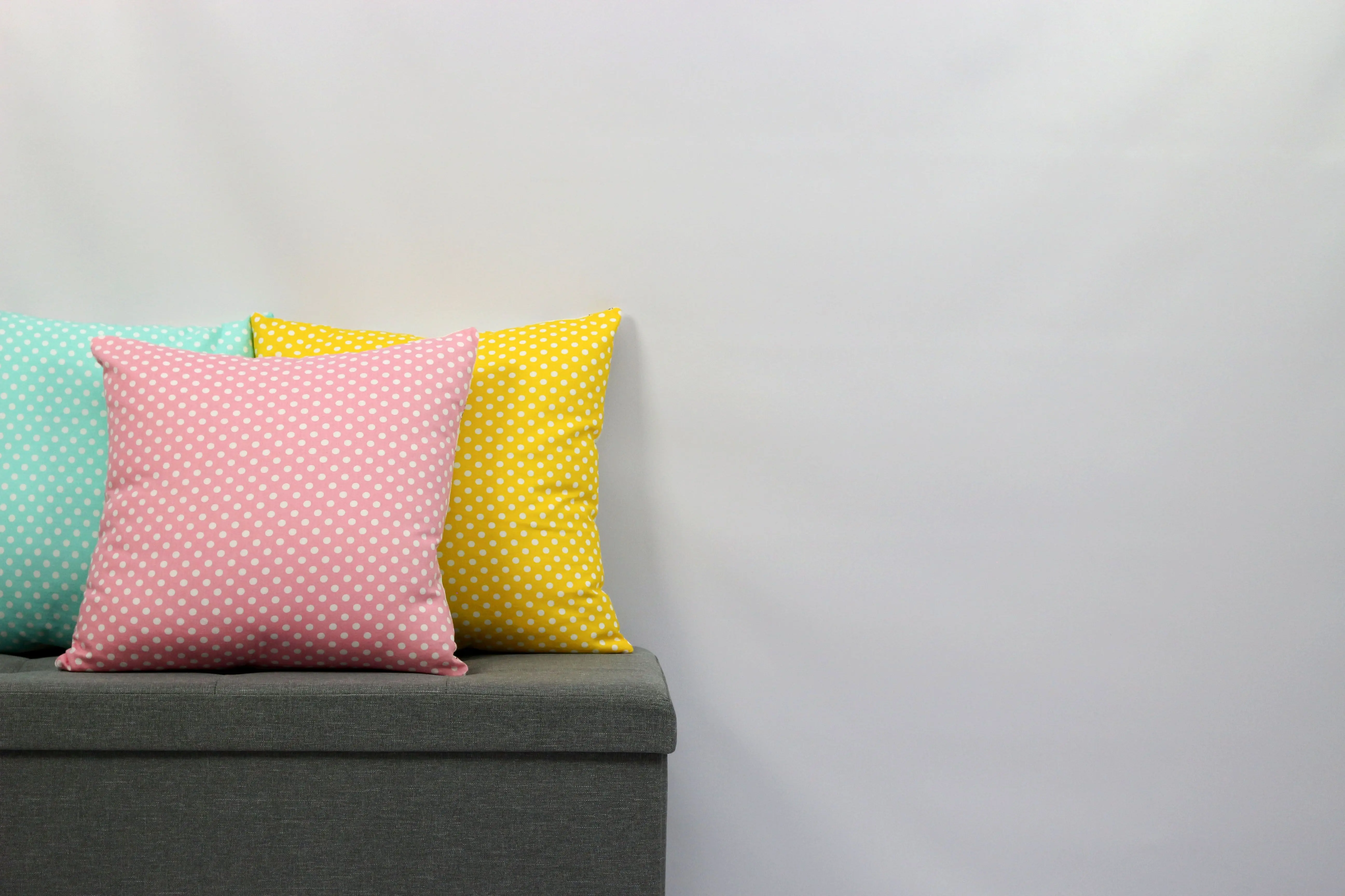 yellow throw pillows Three vibrant polka dot pillows on a grey sofa with a minimalistic background.