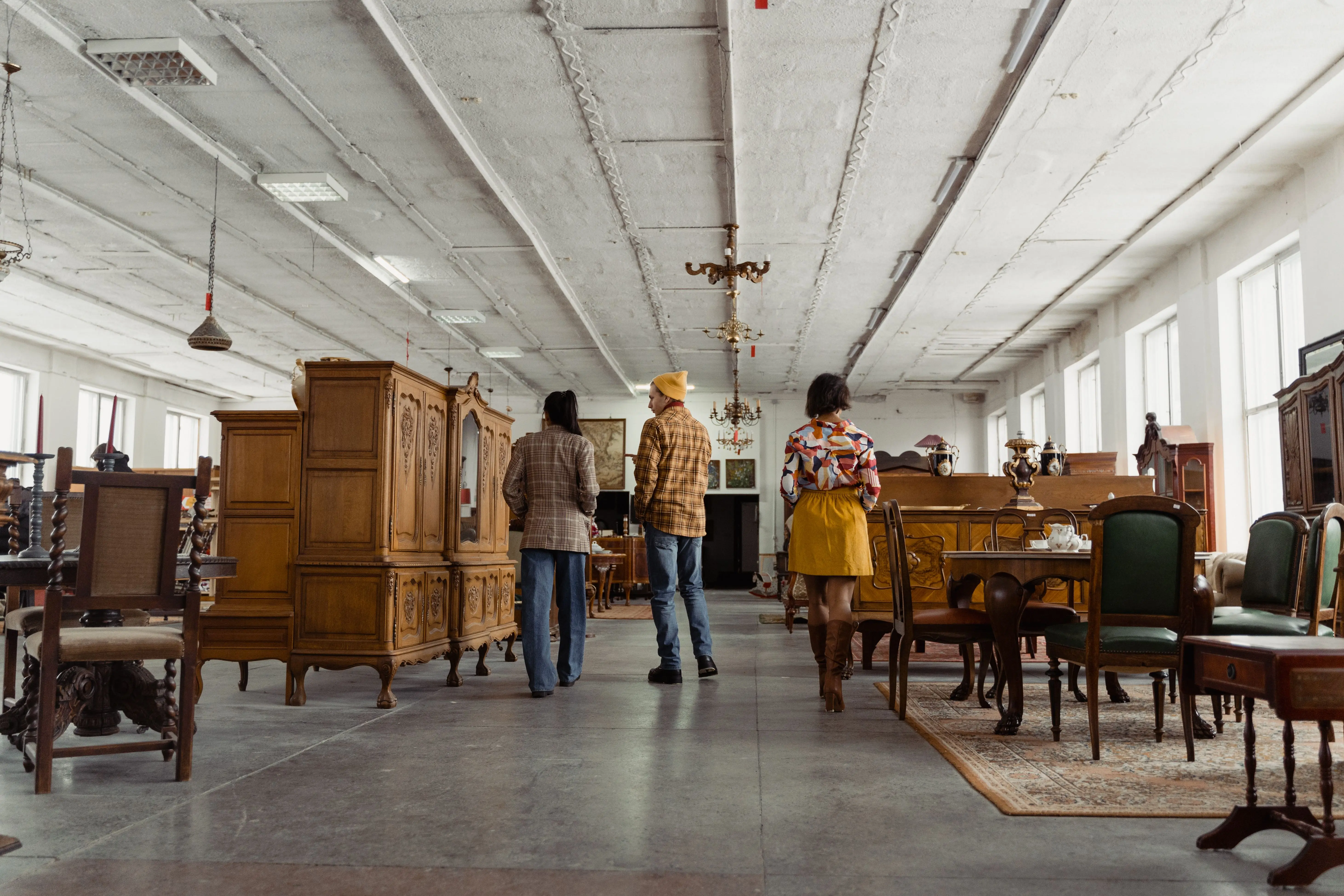 solid wood armoire wardrobe Three people browsing vintage wooden furniture in a spacious store interior with high ceilings.