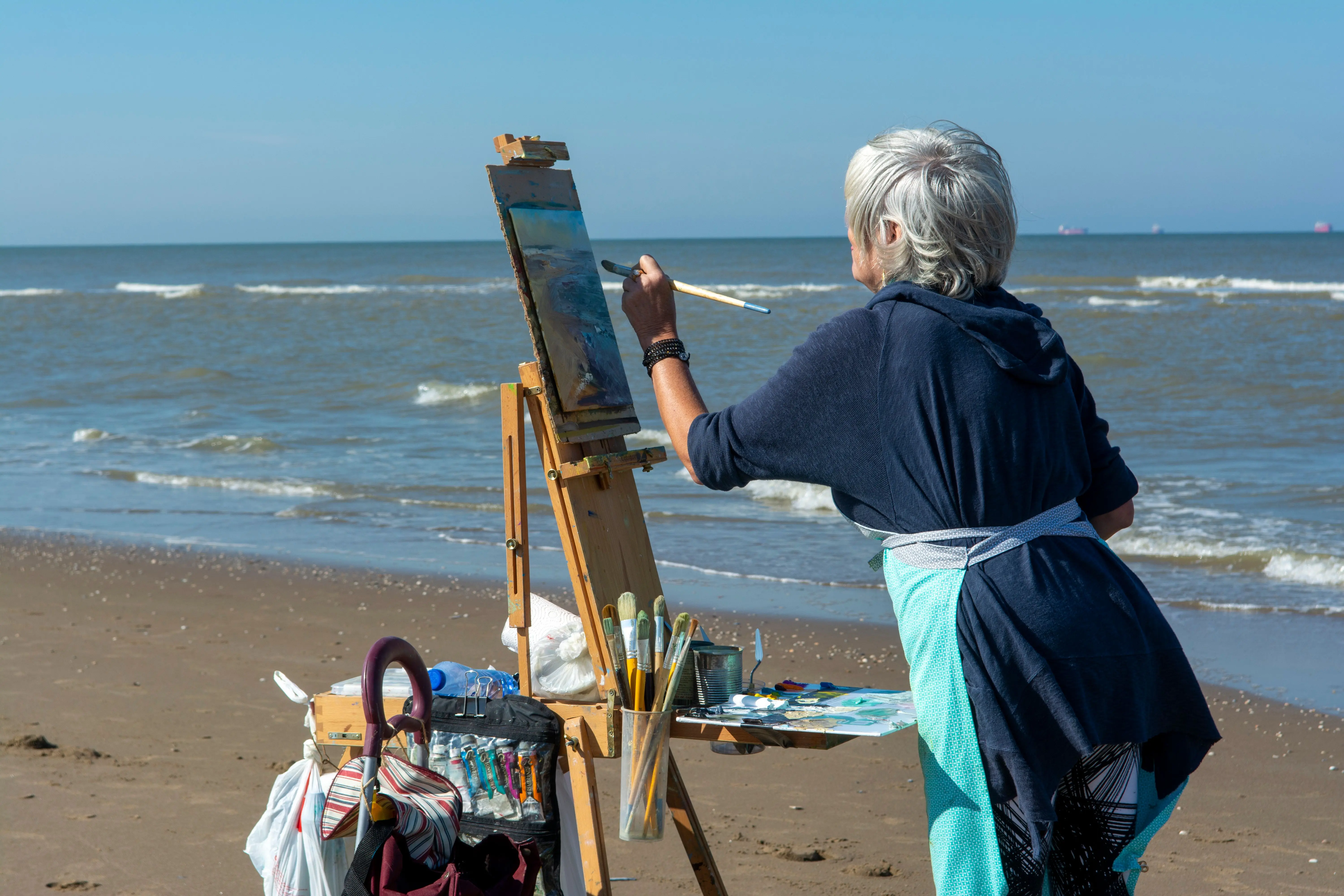 beach wall art Senior woman artist painting on a beach during summer. Creative outdoor art.