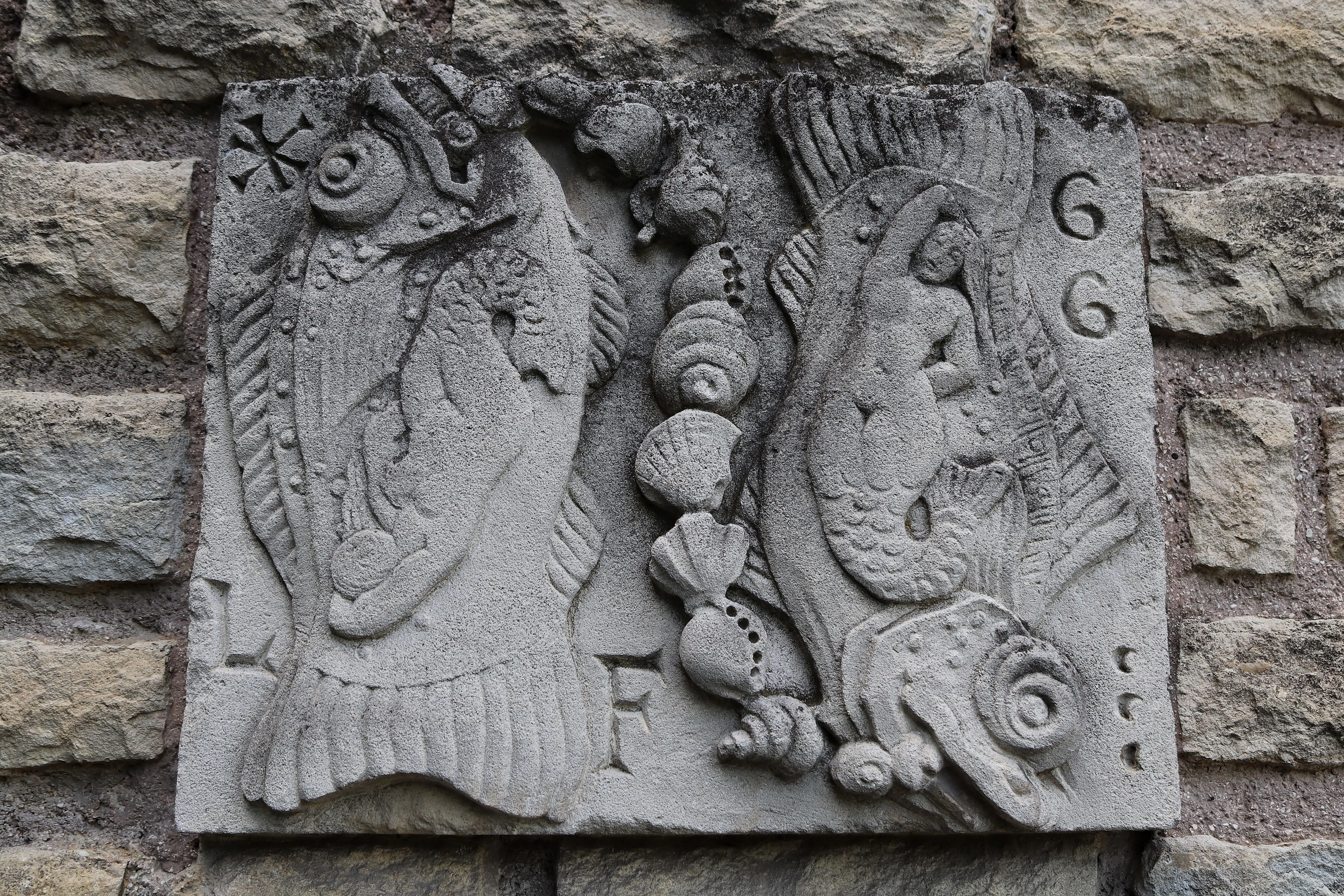 beach wall art Close-up of a stone relief sculpture featuring fish, mermaid, and shell motifs on a textured wall.
