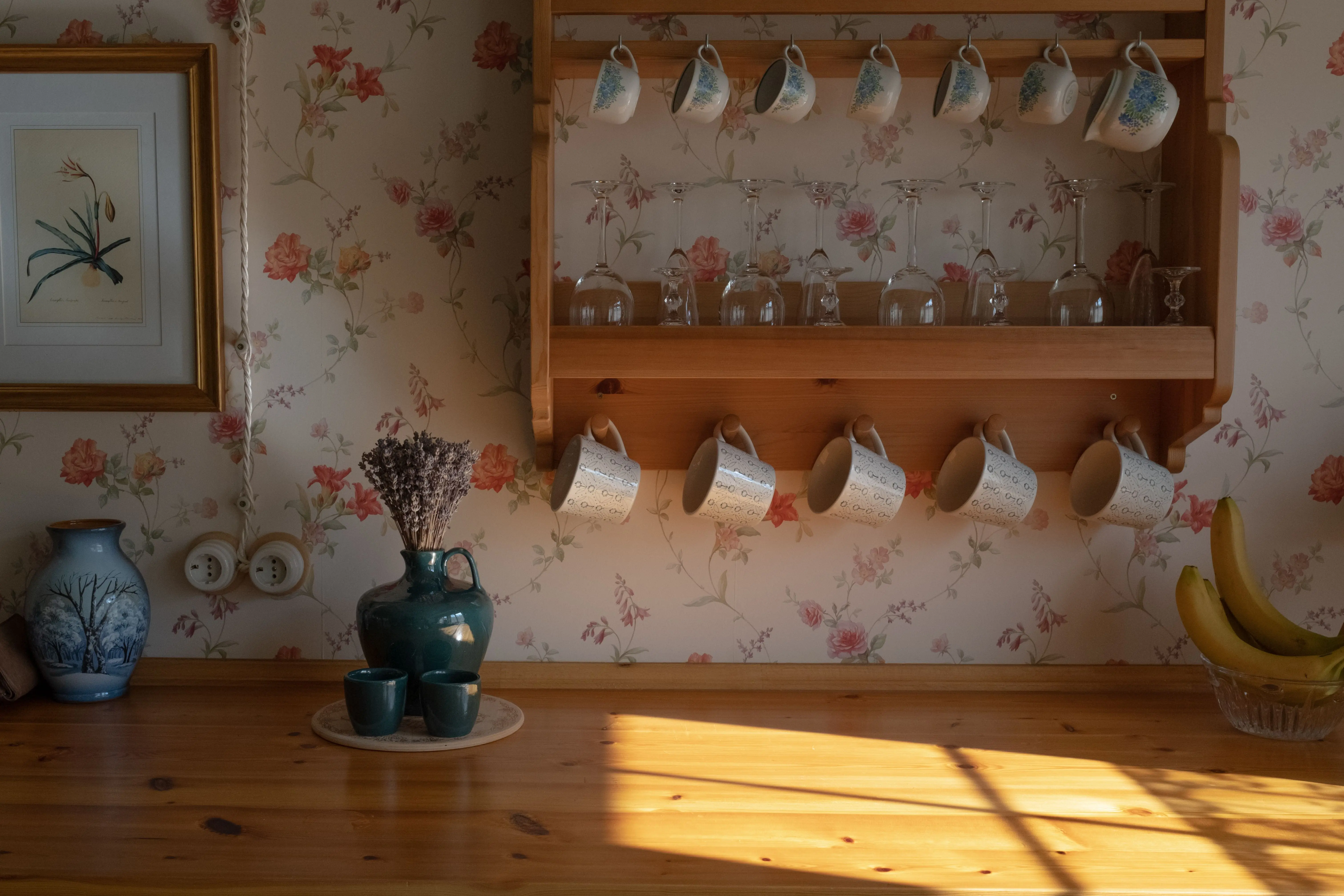 wood wall shelf Vintage kitchen scene with floral mugs on a wooden shelf, sunlight casting warm shadows.