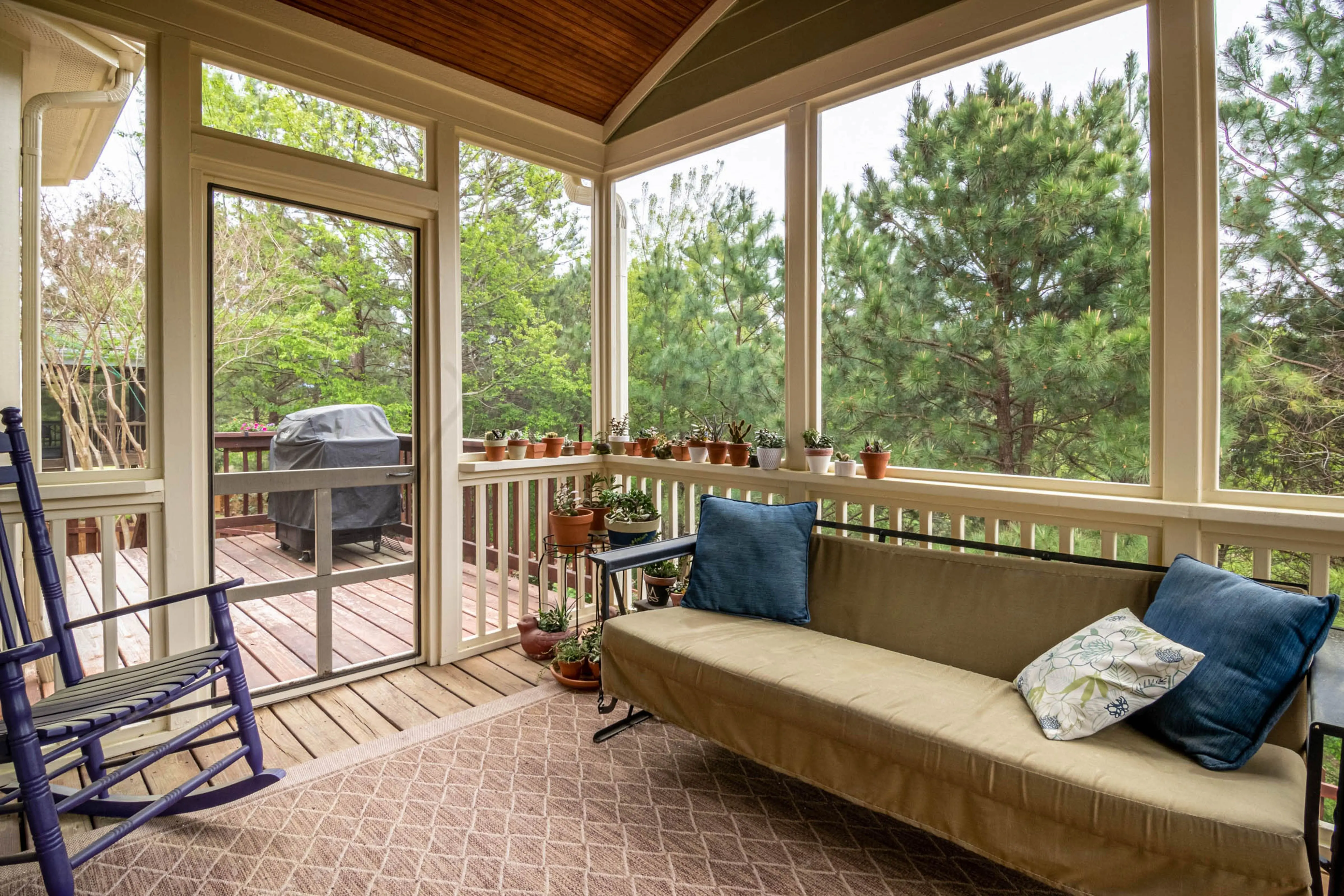 screened in deck Relaxing screened porch with couch, plants, and outdoor greenery view.