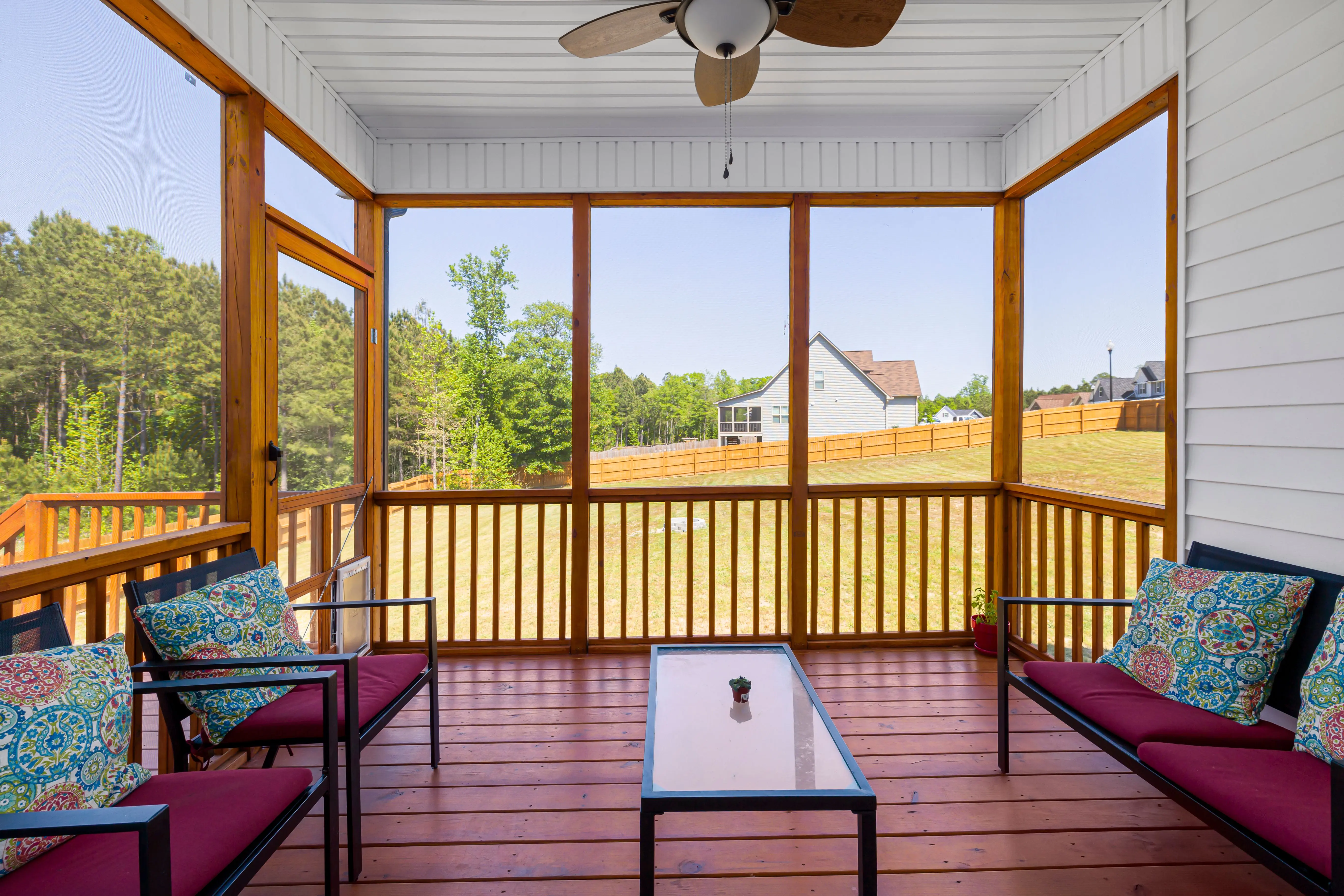 screened in deck An inviting enclosed porch with cozy furniture overlooking lush greenery on a sunny day.