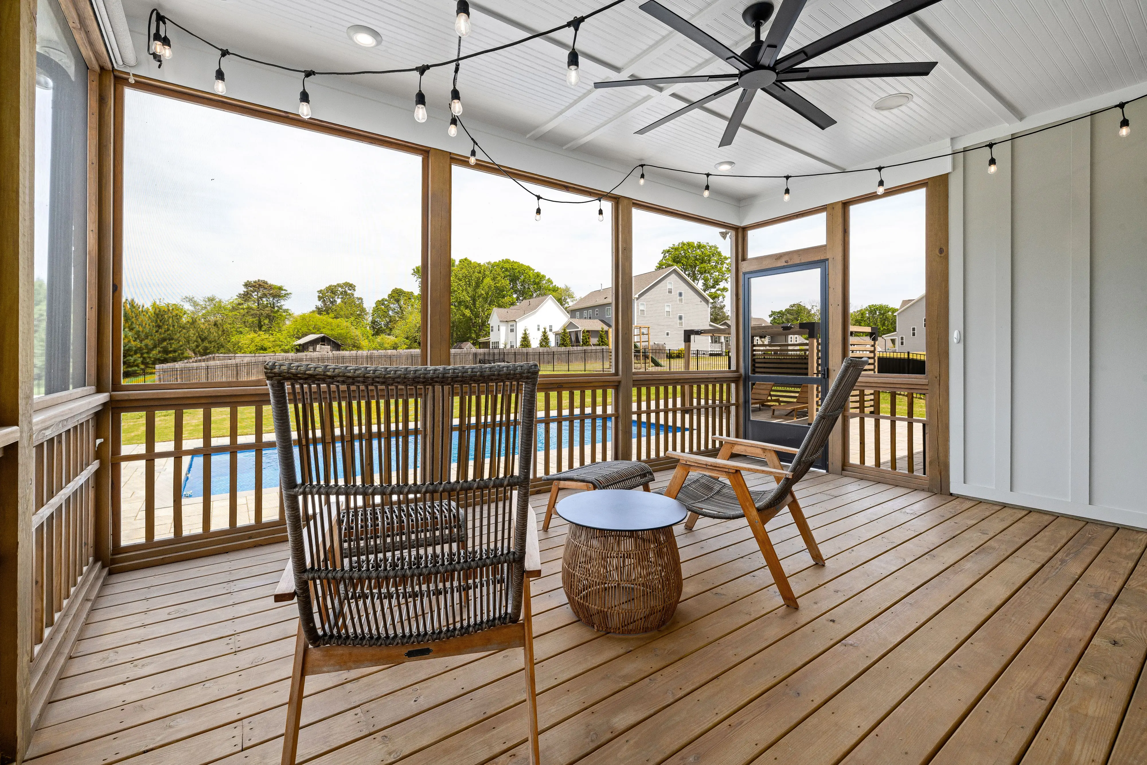 screened in deck Stylish screened terrace with wooden furniture and ceiling fan, overlooking a serene backyard pool.