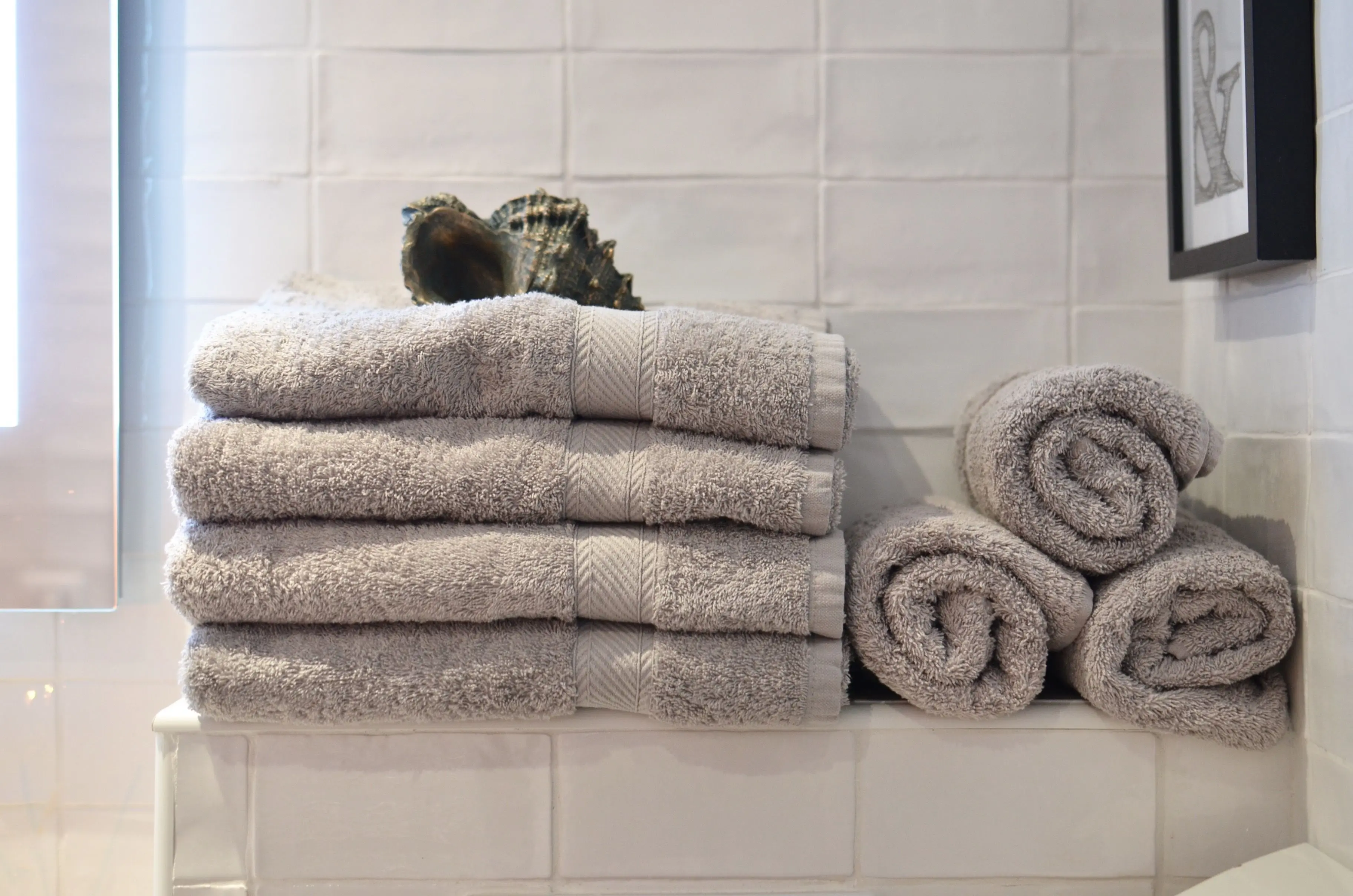 vanity shelves Big shell placed on heap of soft gray towels arranged on shelf near white tiled wall in modern bathroom
