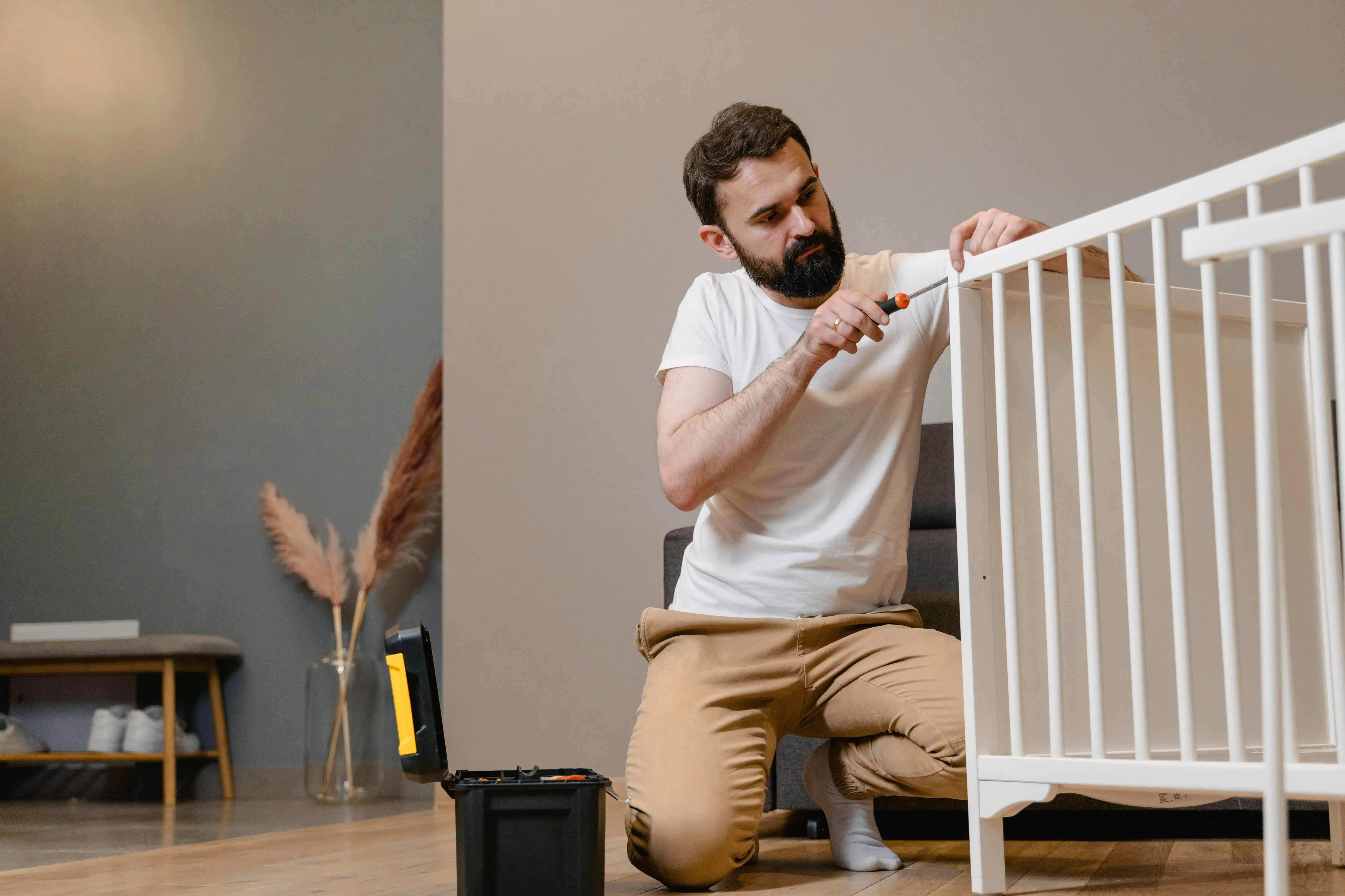 twin platform bed with storage Father kneels to fix a white baby crib using a screwdriver in a contemporary nursery setting.