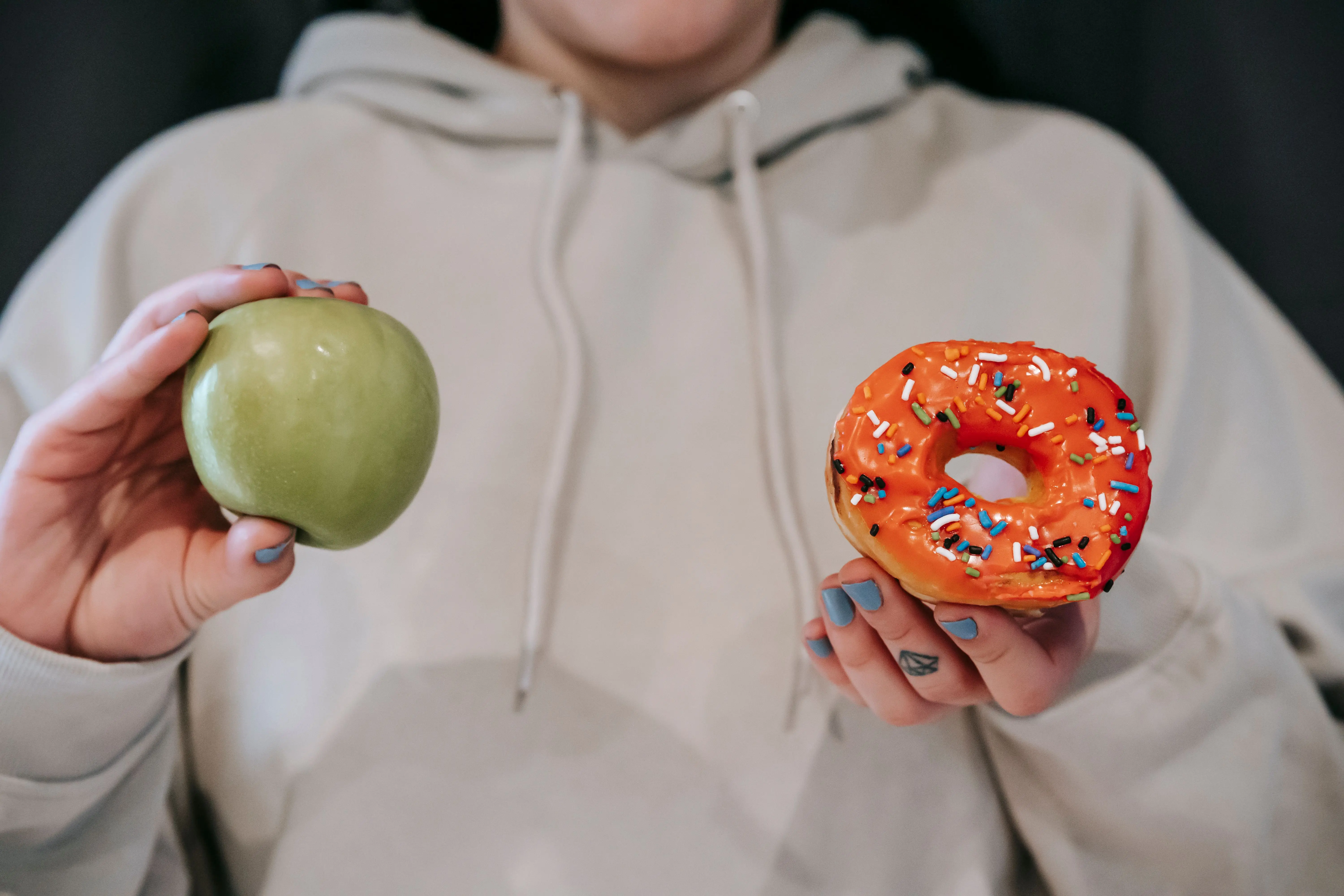 spider bite vs mosquito Crop unrecognizable female in loose hoodie showing healthy green apple and sweet delicious donut