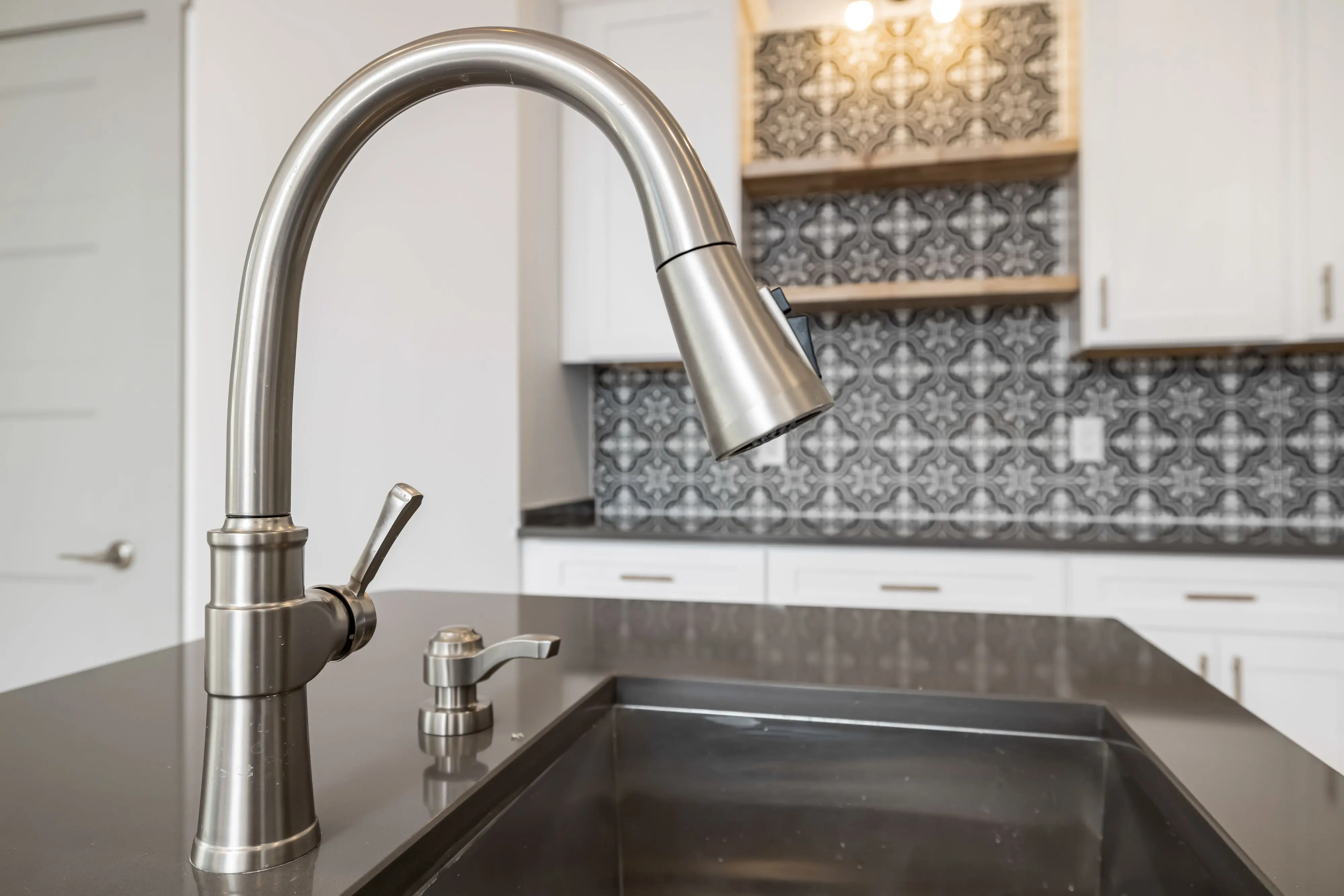 black backsplash Close-up view of a modern stainless steel kitchen faucet with sleek design against tiled backsplash.