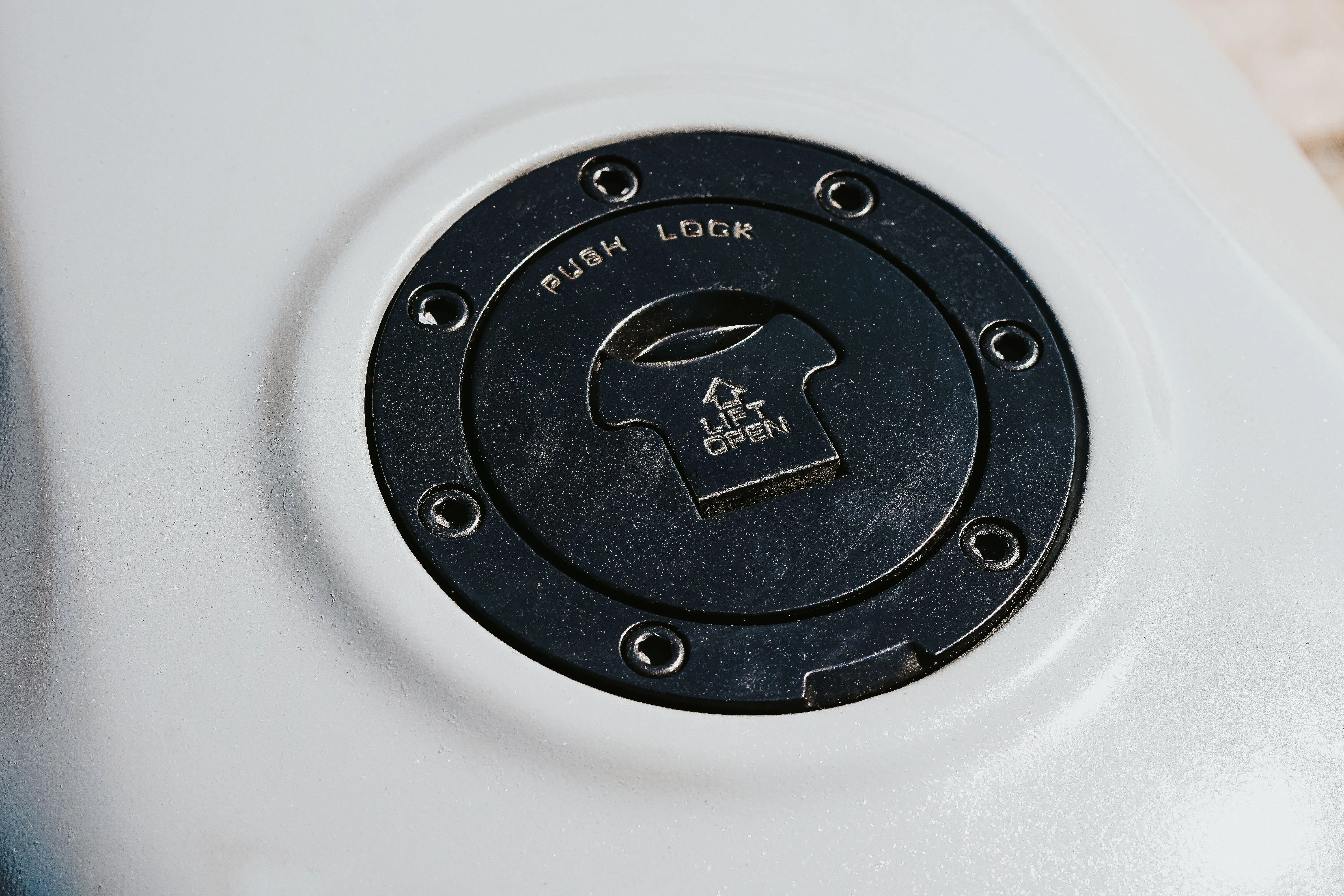 black cabinet hardware Detailed view of a black push lock fuel cap with lift to open instructions.